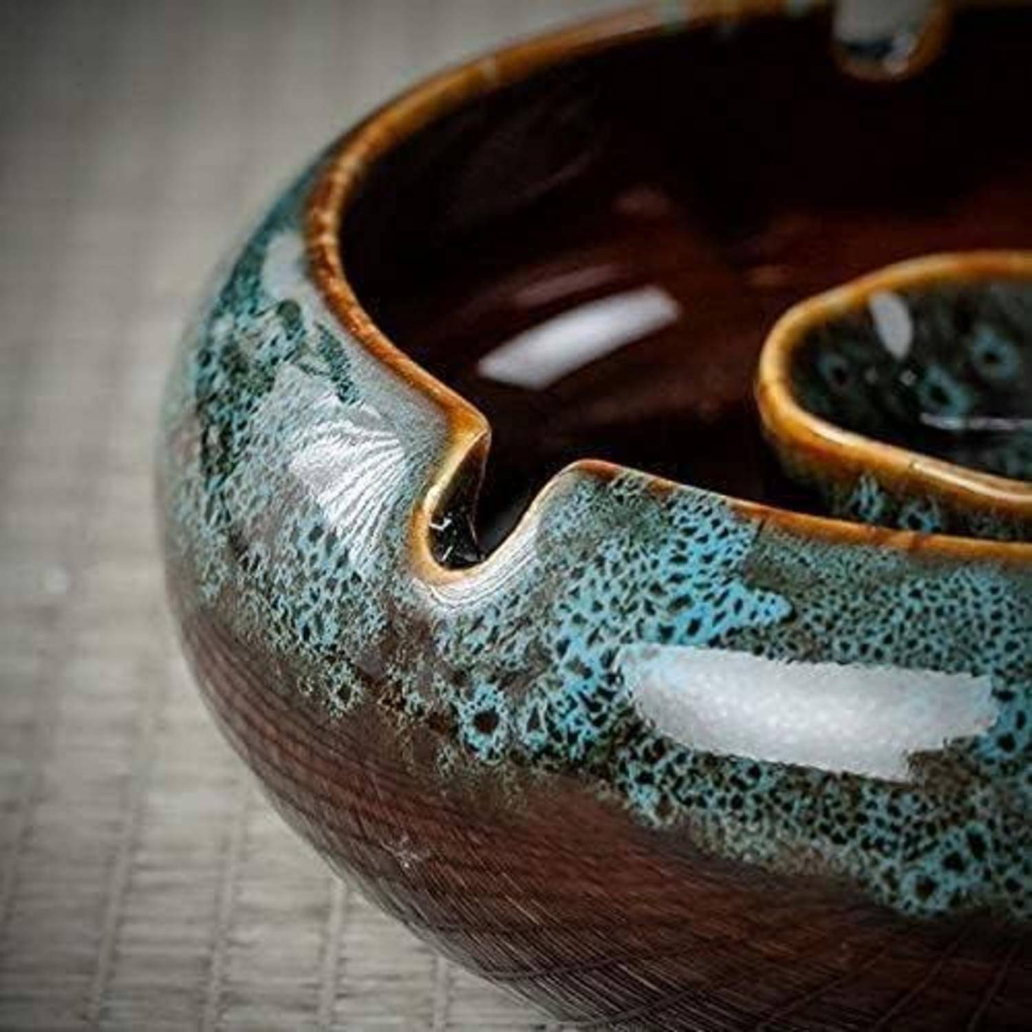 Nahaufnahme einer strukturierten Keramikschale mit glänzender blaugrüner und brauner Glasur, von oben auf einer neutralen Oberfläche gezeigt.