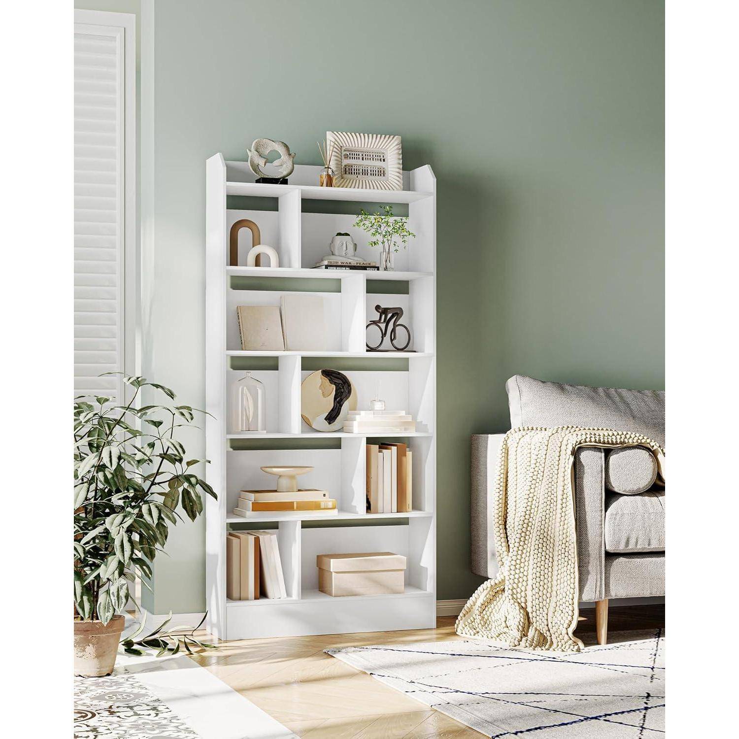 Weißes Bücherregal mit Dekor und Büchern in einem hellen Wohnzimmer neben einem Sofa mit einer Wurfdecke und einer Topfpflanze.
