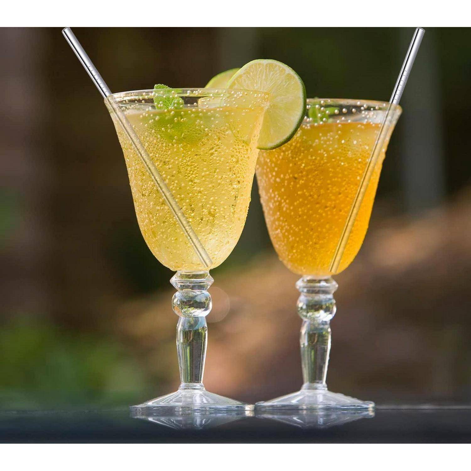 Zwei funkelnde Limetten-Cocktails in Stielgläsern mit Strohhalmen, einer mit einer Limettenscheibe garniert, vor einem unscharfen Hintergrund.