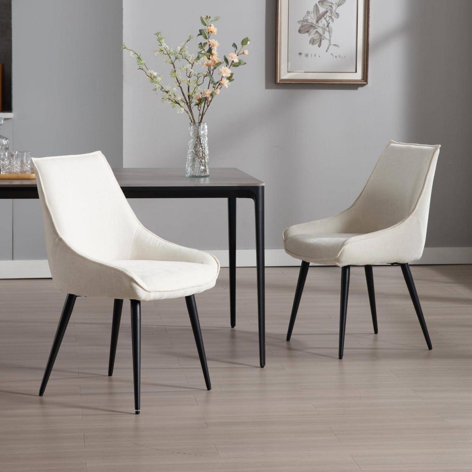 Zwei moderne gepolsterte Esszimmerstühle mit schwarzen Beinen stehen neben einem dunklen Tisch in einem grauen Esszimmer mit einer Vase mit Blumen und Wandkunst.
