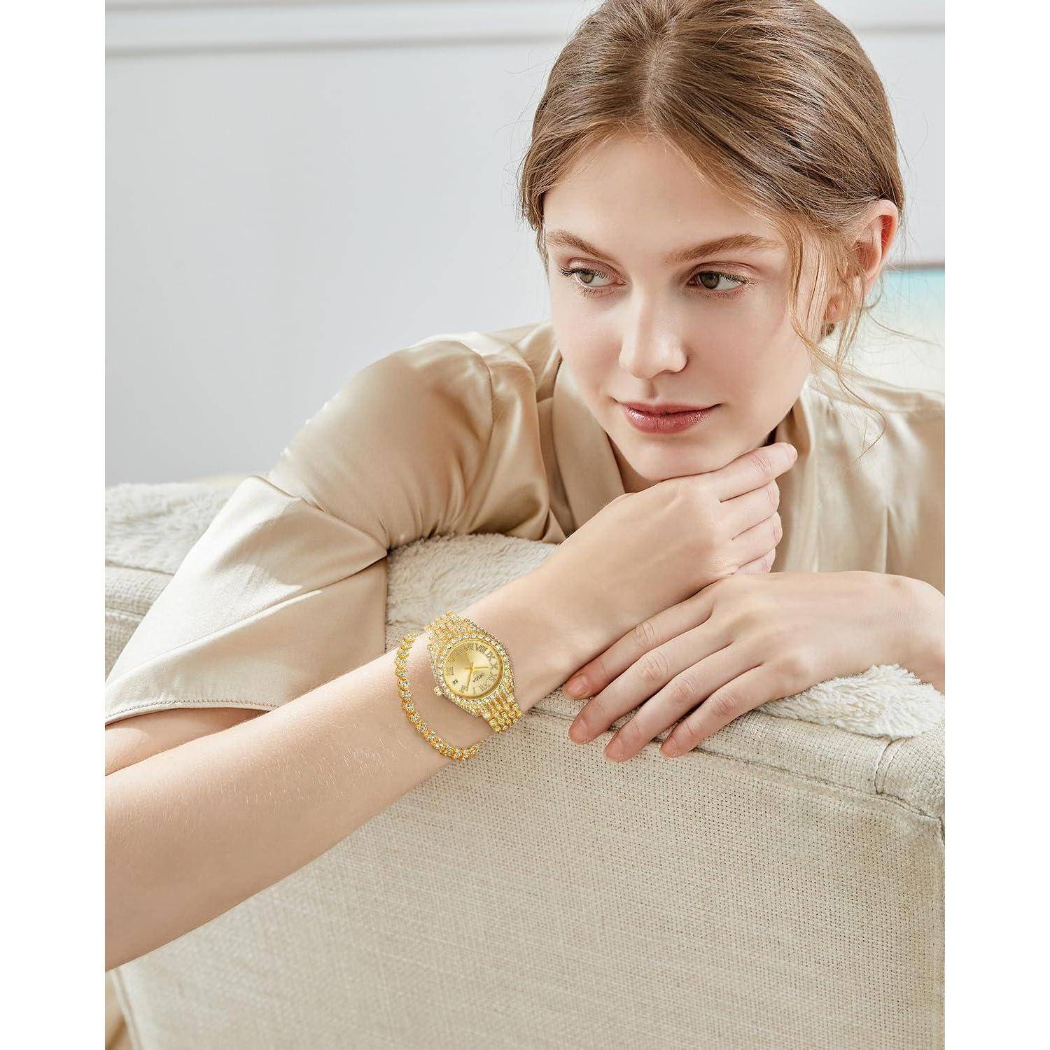 Frau in einer beigen Bluse lehnt sich auf einem Sofa an, trägt eine goldene Armbanduhr und ein Armband und blickt nachdenklich zur Seite.
