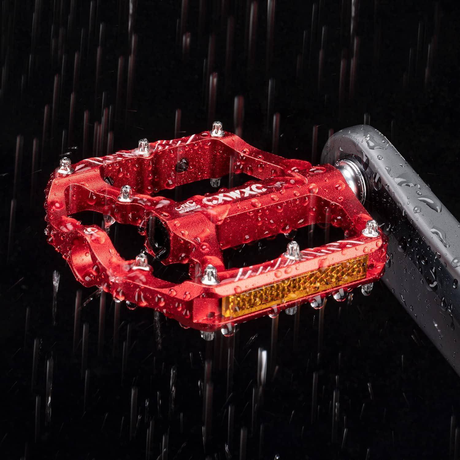 Großaufnahme eines roten Metallfahrradpedals mit Wassertropfen und Regen, die gegen einen dunklen Hintergrund spritzen.