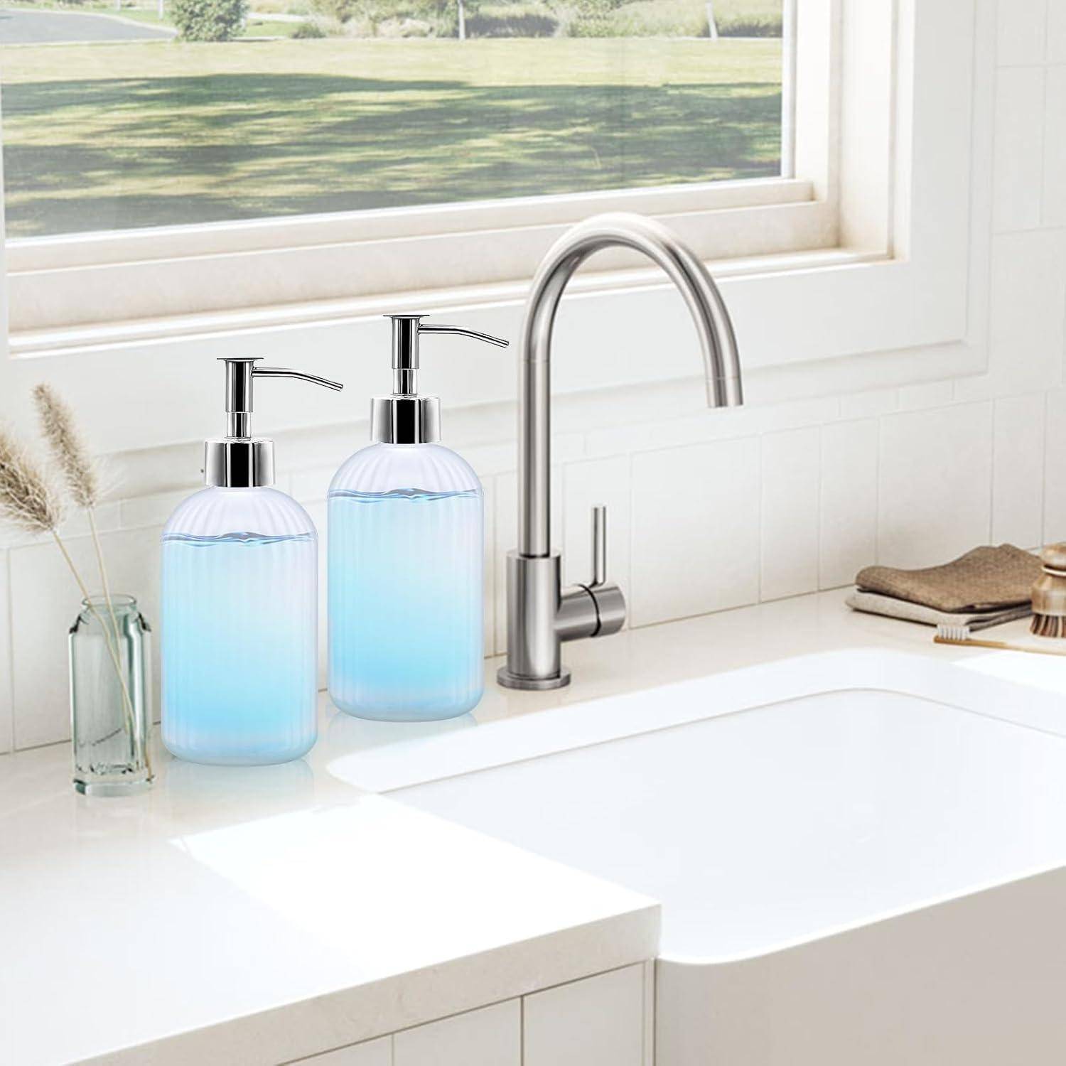 Helles Küchenspülbecken mit Edelstahlarmatur, zwei blaue Seifenspender, eine kleine Vase und gefaltete Tücher auf der Arbeitsplatte neben einem Fenster.