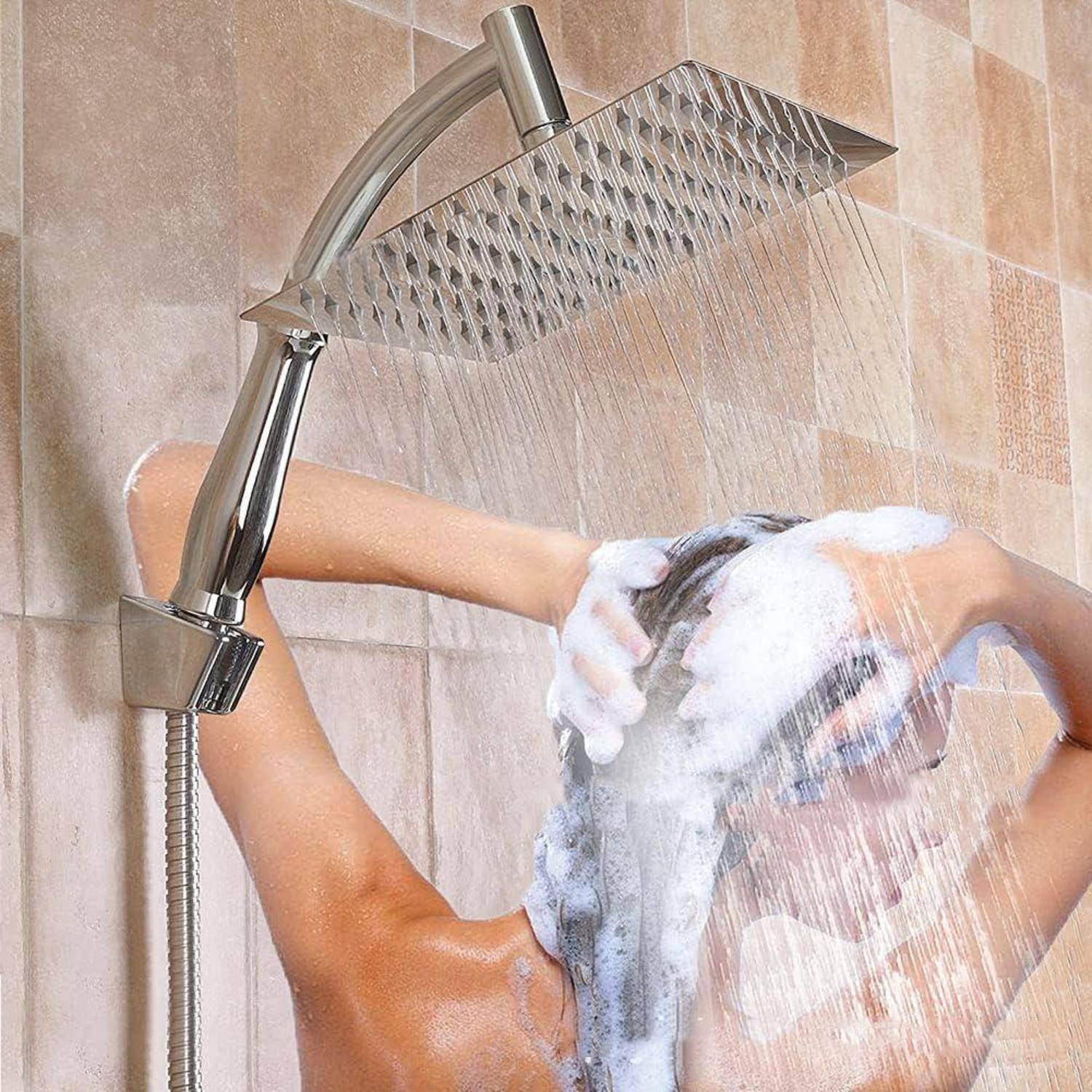 Person wäscht sich die Haare unter einem großen Duschkopf, mit Shampoo-Schaum und Wasser, das in einer gefliesten Dusche strömt.