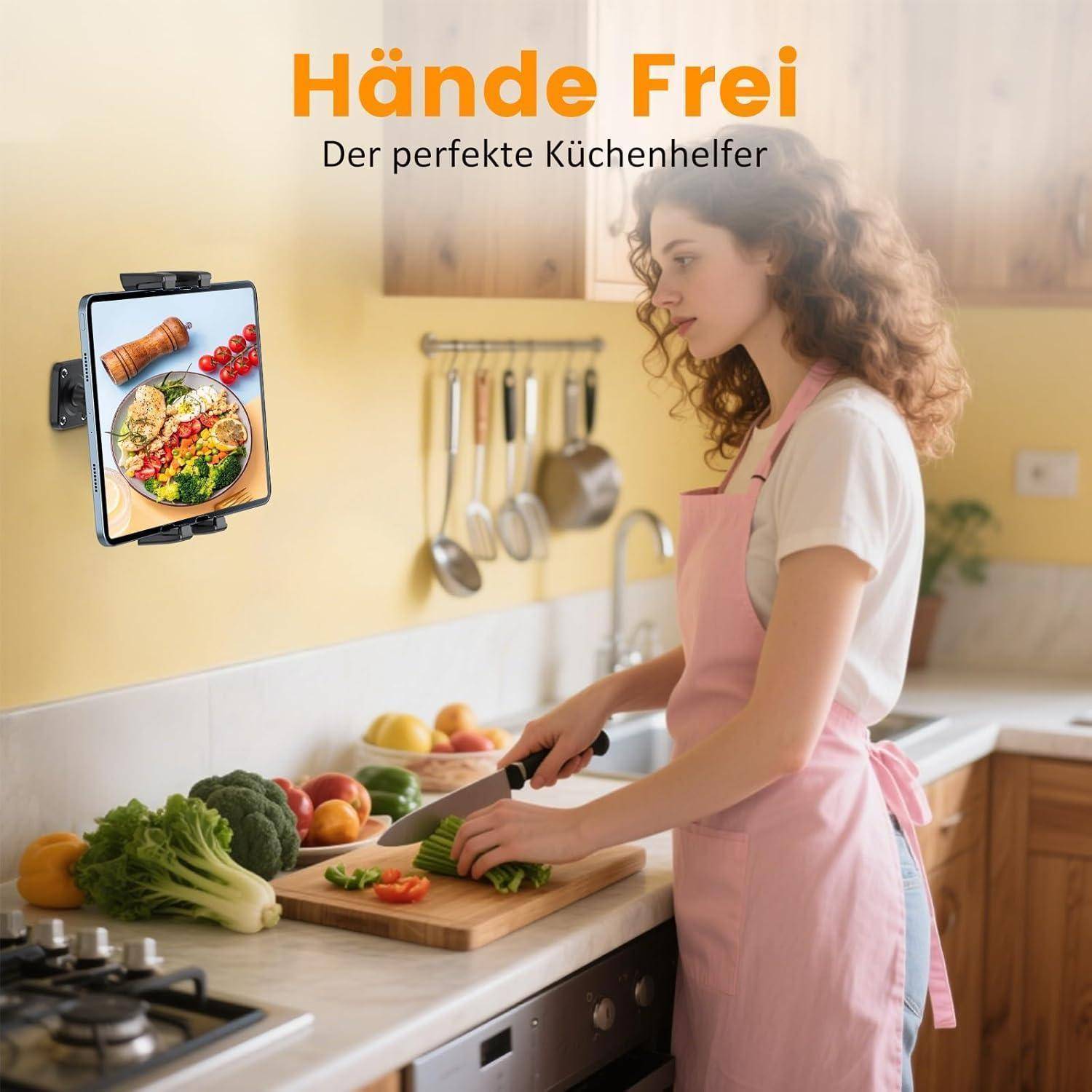 Werbung für „Hände Frei" Küchenhelfer: Eine Frau in pinker Schürze hackt Gemüse, während ein an der Wand montiertes Tablet ein Rezeptbild anzeigt.