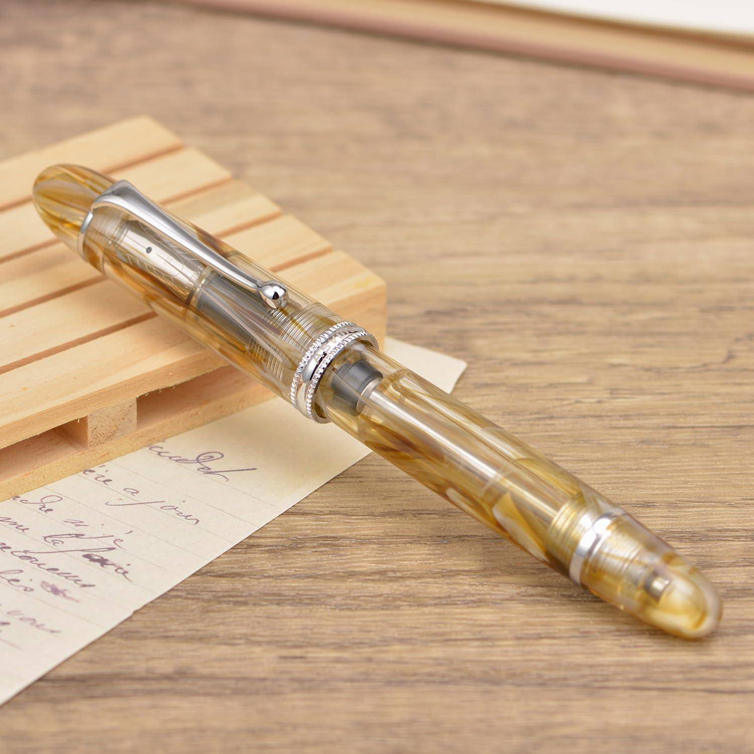 Transparenter bernsteinfarbener Füller liegt diagonal auf einem Holzschreibtisch neben einer handschriftlichen Notiz und einem kleinen Holzständer.
