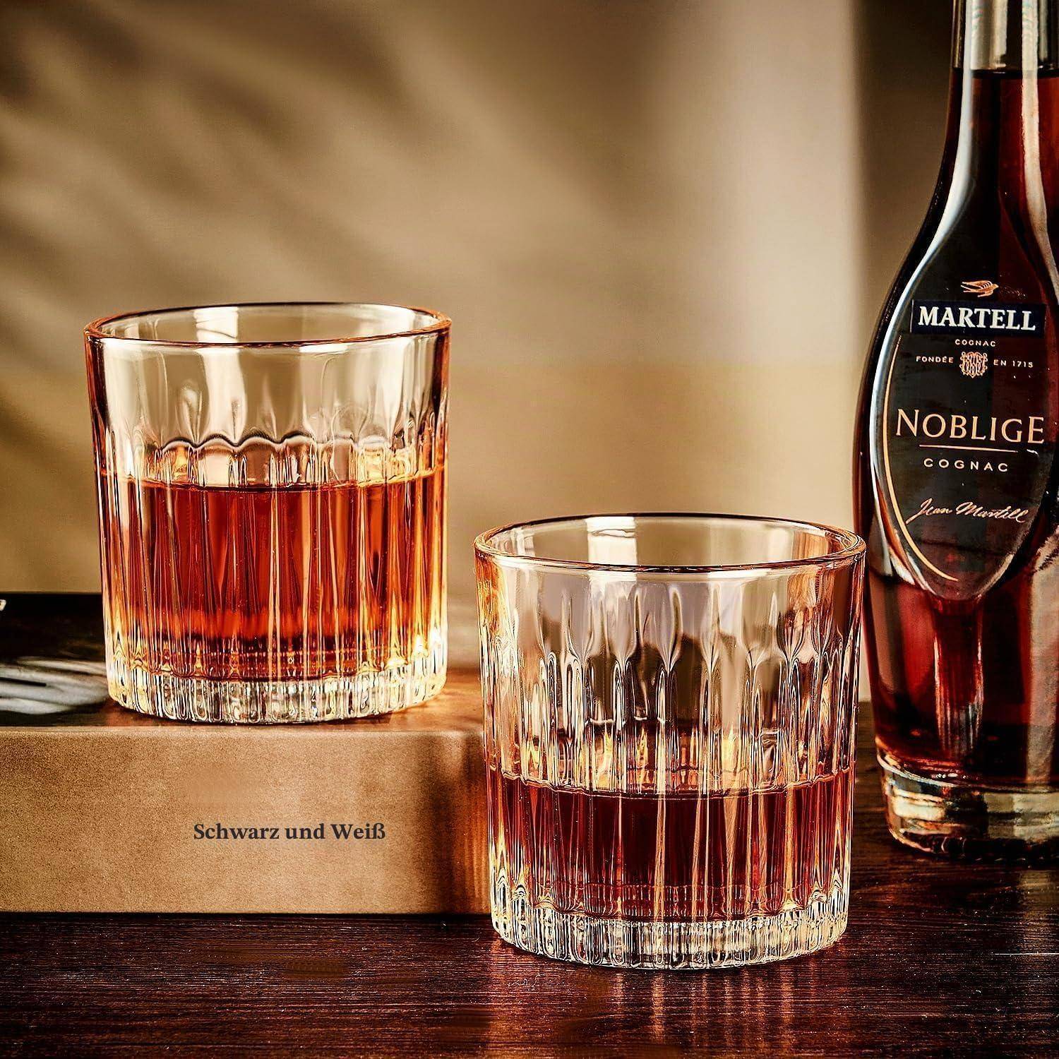 Zwei Kristallgläser mit Cognac neben einer Flasche Martell Noblige auf einer braunen Box mit der Aufschrift „Schwarz und Weiß