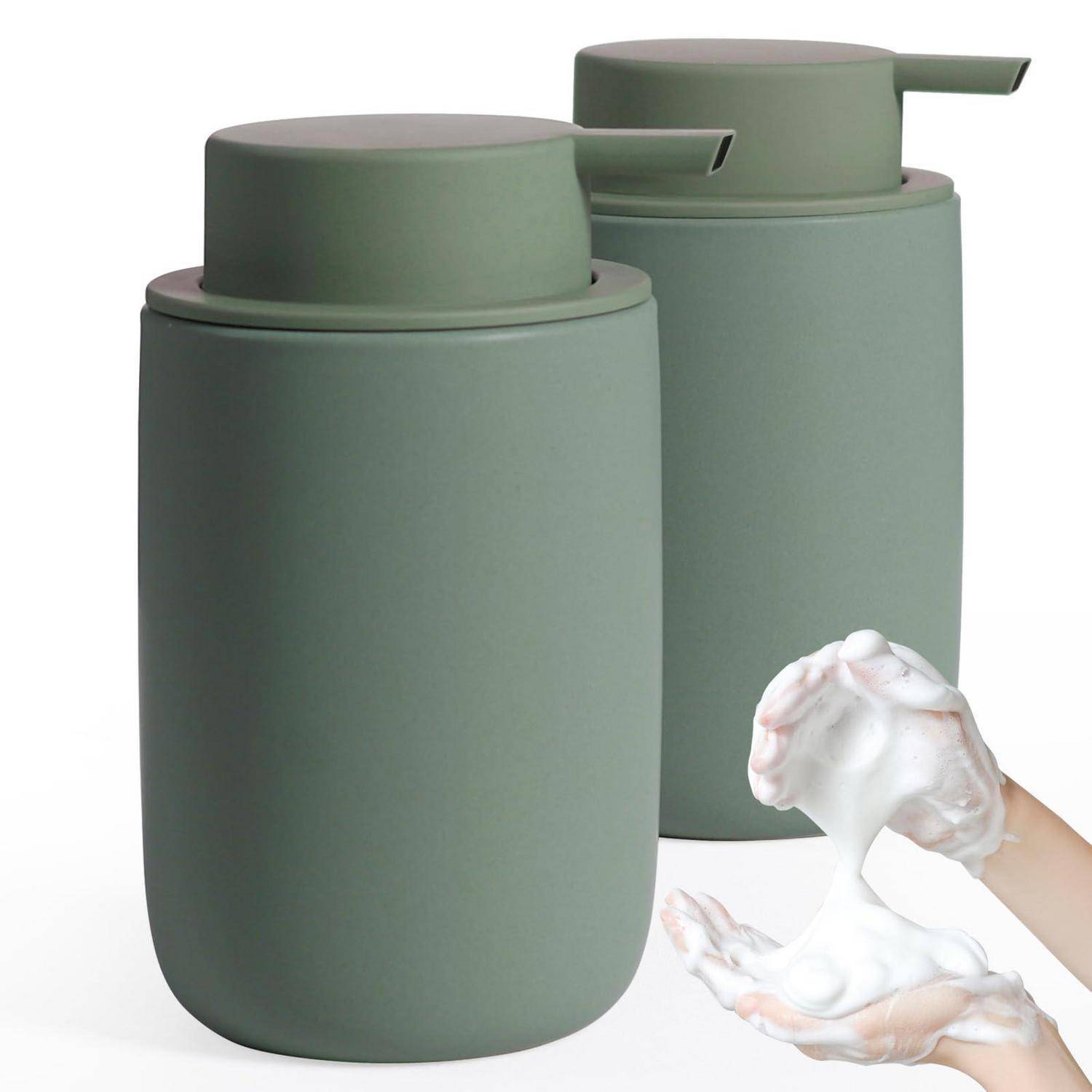 Zwei matte grüne Pumpspender für Seife oder Lotion, mit einer Hand, die weißen Schaum davor hält.