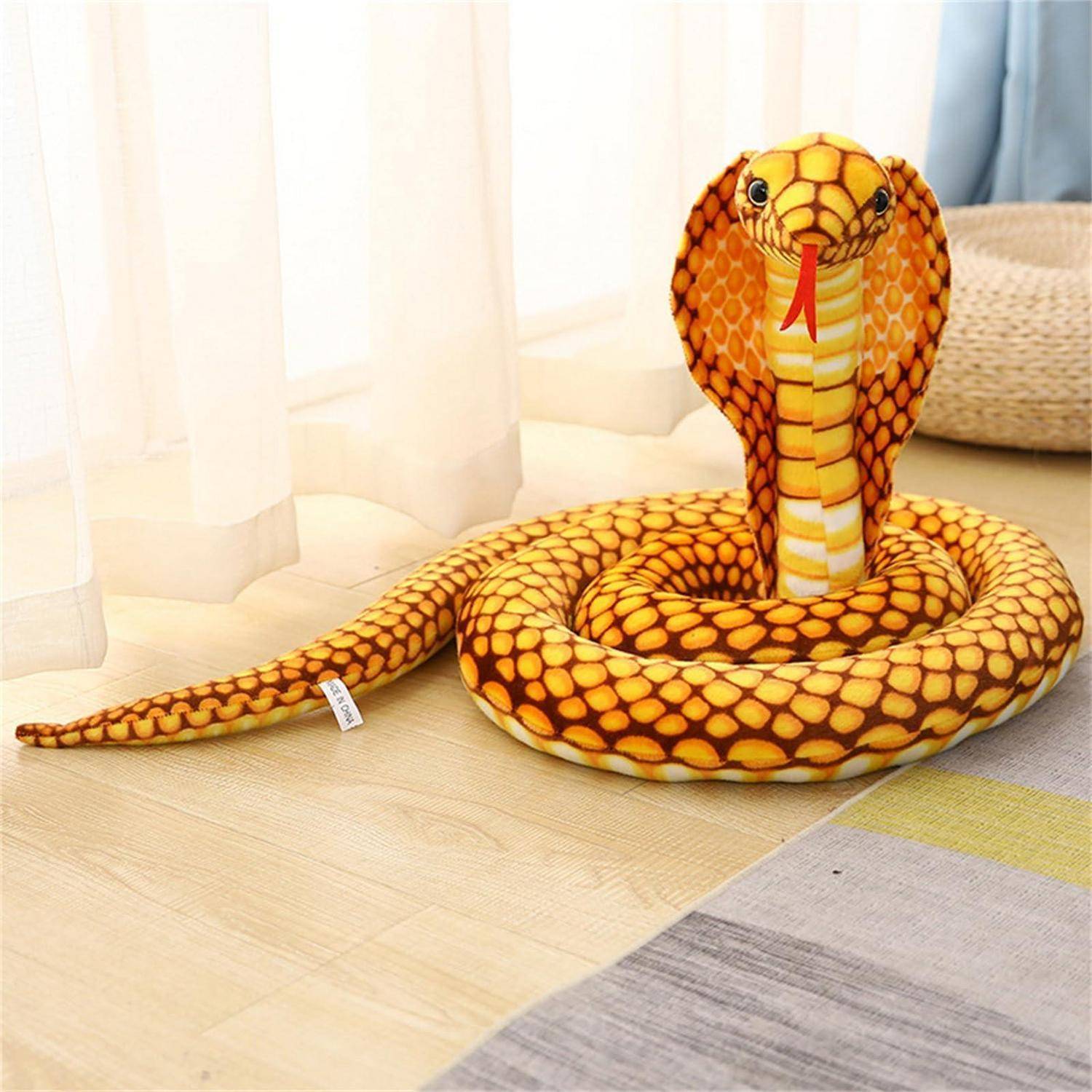 Kuschel-Kobra-Schlangenfigur aufgerollt auf einem Boden in einem hellen Raum, mit aufgerichteter Haube und herausgestreckter Zunge.