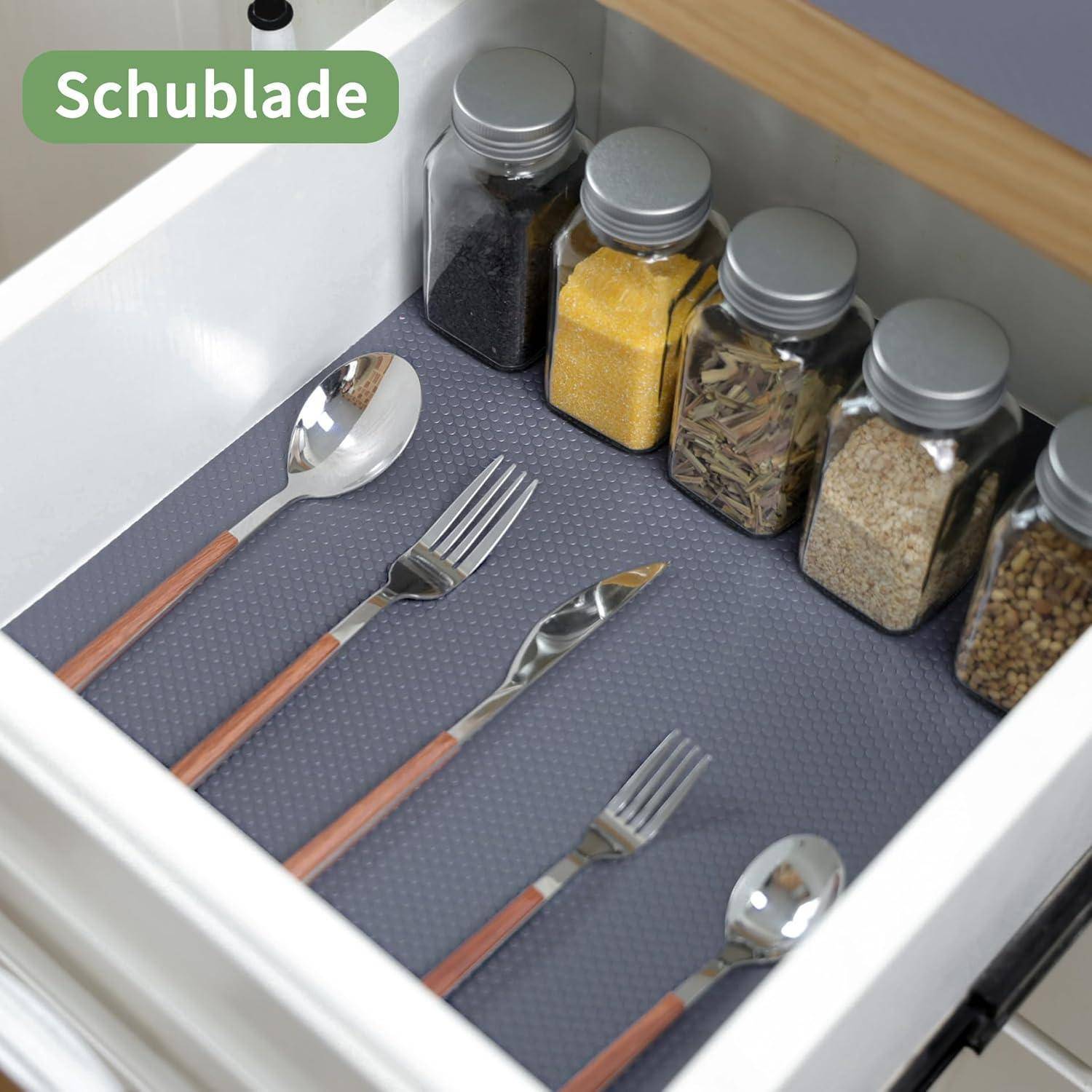 Öffne die Schublade mit einer grauen Rutschschutzunterlage, die Besteck und Gewürzgläser hält; mit der Bezeichnung 