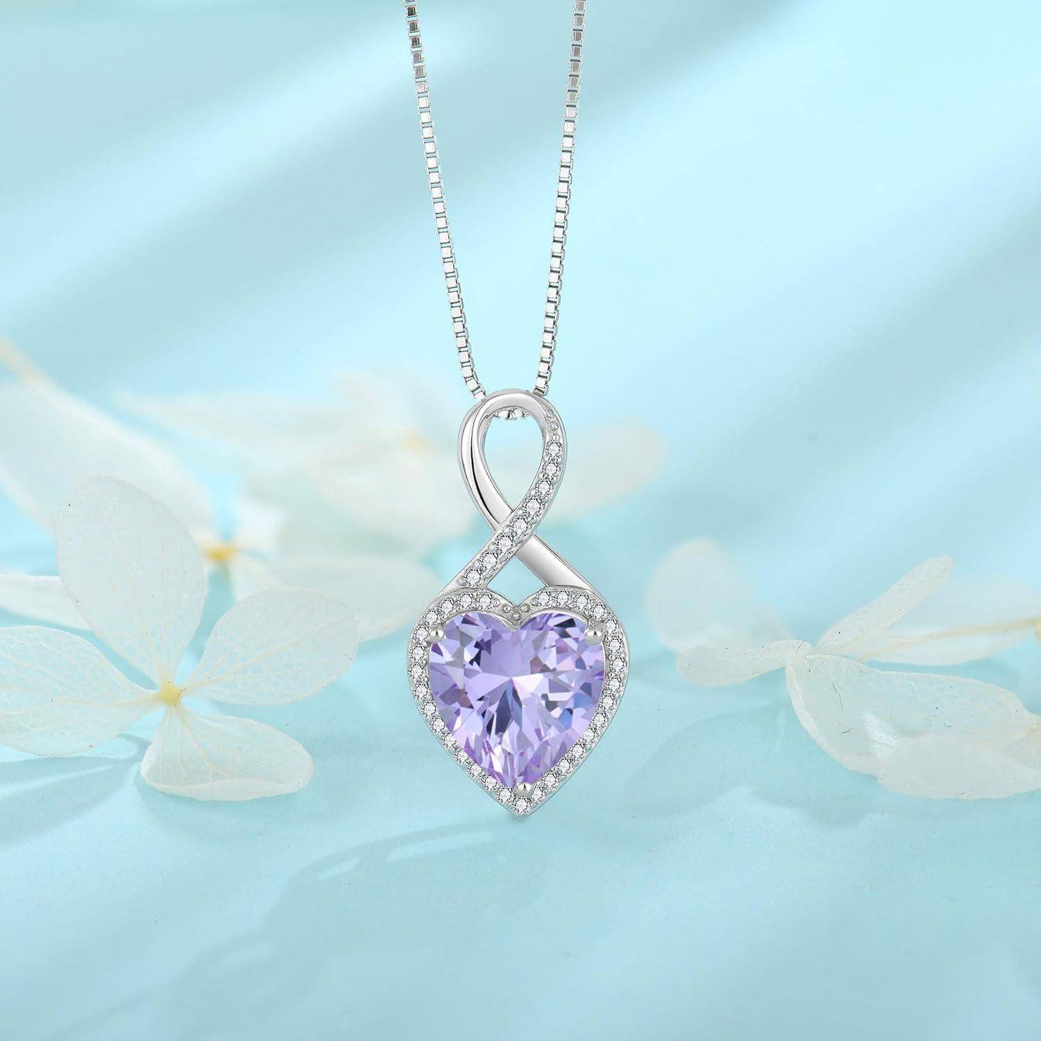 Herzförmiger violetter Edelsteinanhänger an einer Silberkette, umrahmt von einer glitzernden Schleife und vor einem weichen blauen Blumenhintergrund angebracht.