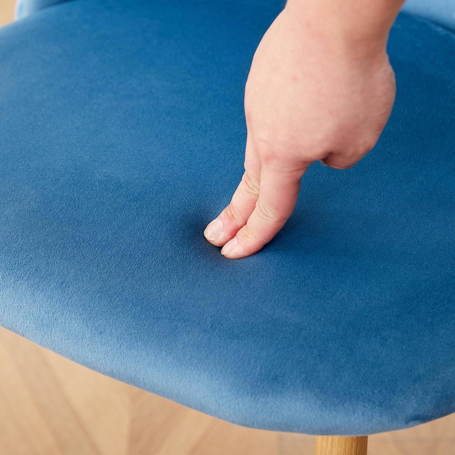 Eine Hand drückt einen Finger in einen blauen gepolsterten Sitz, wodurch die Weichheit und Elastizität des Materials sichtbar werden.