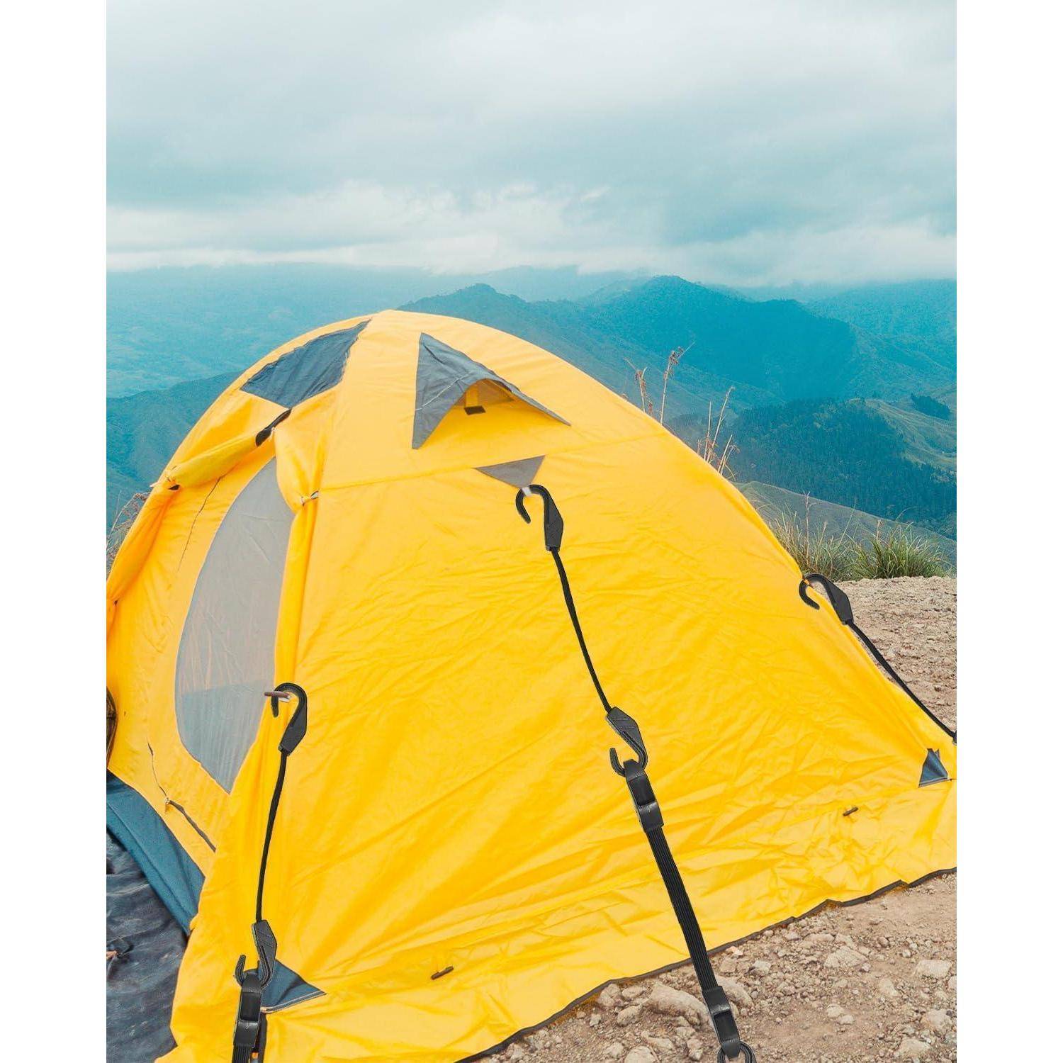 Gelbes Campingzelt auf einem felsigen Berggipfel aufgestellt, mit nebligen blauen Hügeln und bewölktem Himmel im Hintergrund.