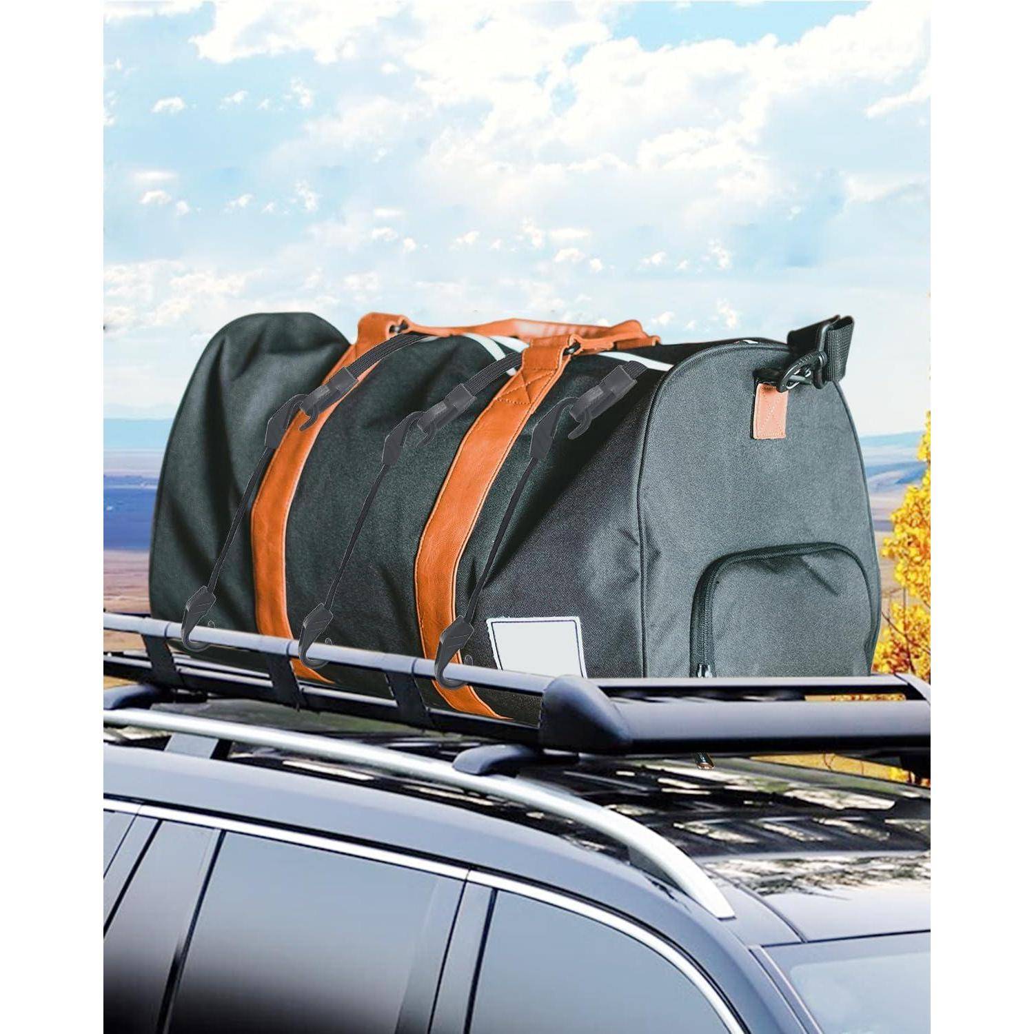 Große graue Reisetasche mit orangefarbenen Riemen, die auf einem Dachgepäckträger eines Autos im Freien befestigt ist.