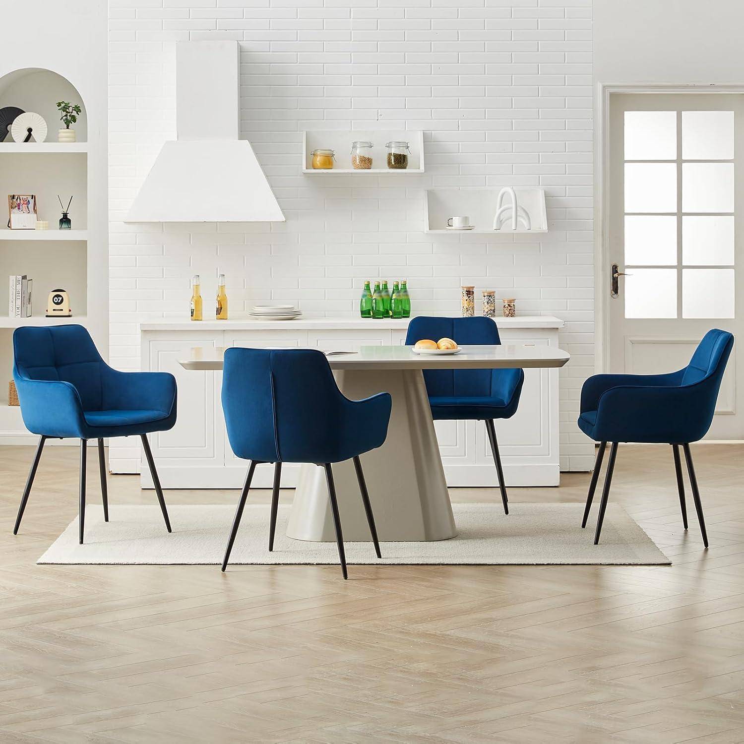 Modernes Esszimmer mit einem weißen Tisch, vier blauen Stühlen, Regalen und einer weißen Backsteinwand mit Küchendekor.
