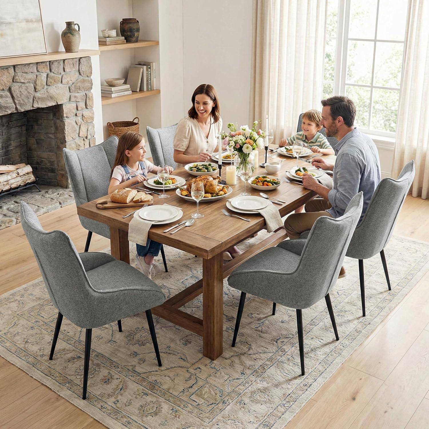 Eine Familie von vier Personen sitzt zusammen am Esstisch in einem hellen Wohnzimmer neben einem Steinkamin, mit Tellern voller Essen und Blumen auf dem Tisch.