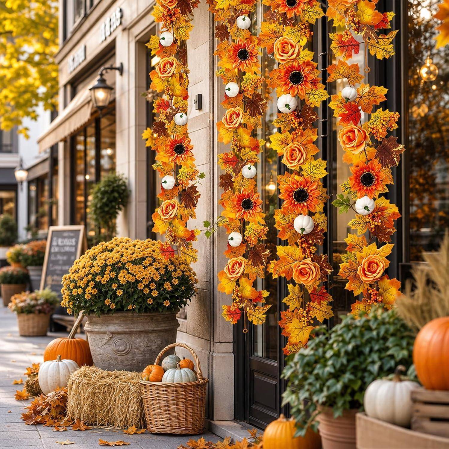 Herbstliche Ladenfront, die mit hängenden orangefarbenen Blumengirlanden, Kürbissen, Heuballen und getopften Chrysanthemen auf einem Gehweg dekoriert ist.