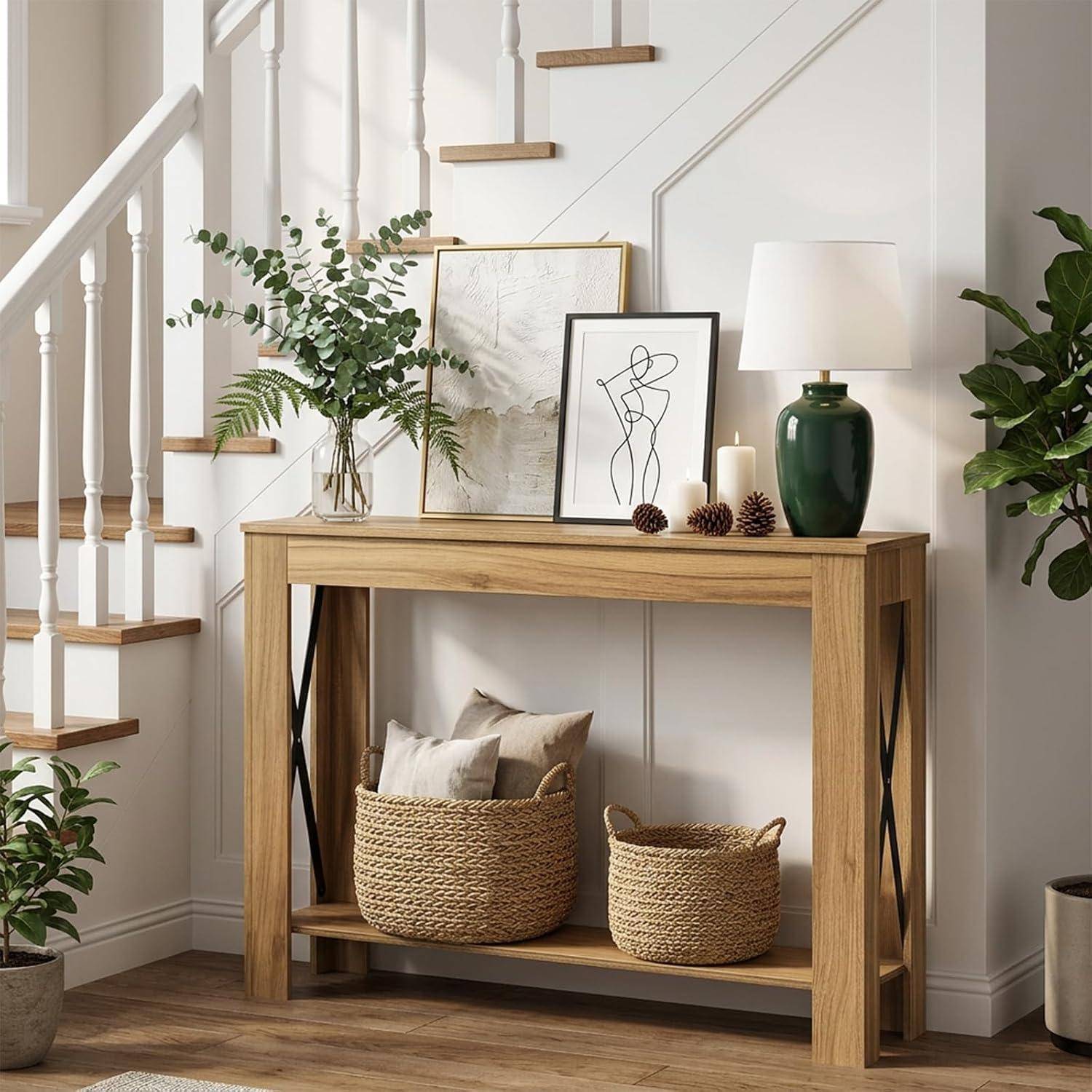 Holzkonsole, die mit gerahmter Kunst, einer Vase, einer Lampe und geflochtenen Körben neben einer Treppe in einem hellen Eingangsbereich gestylt ist.