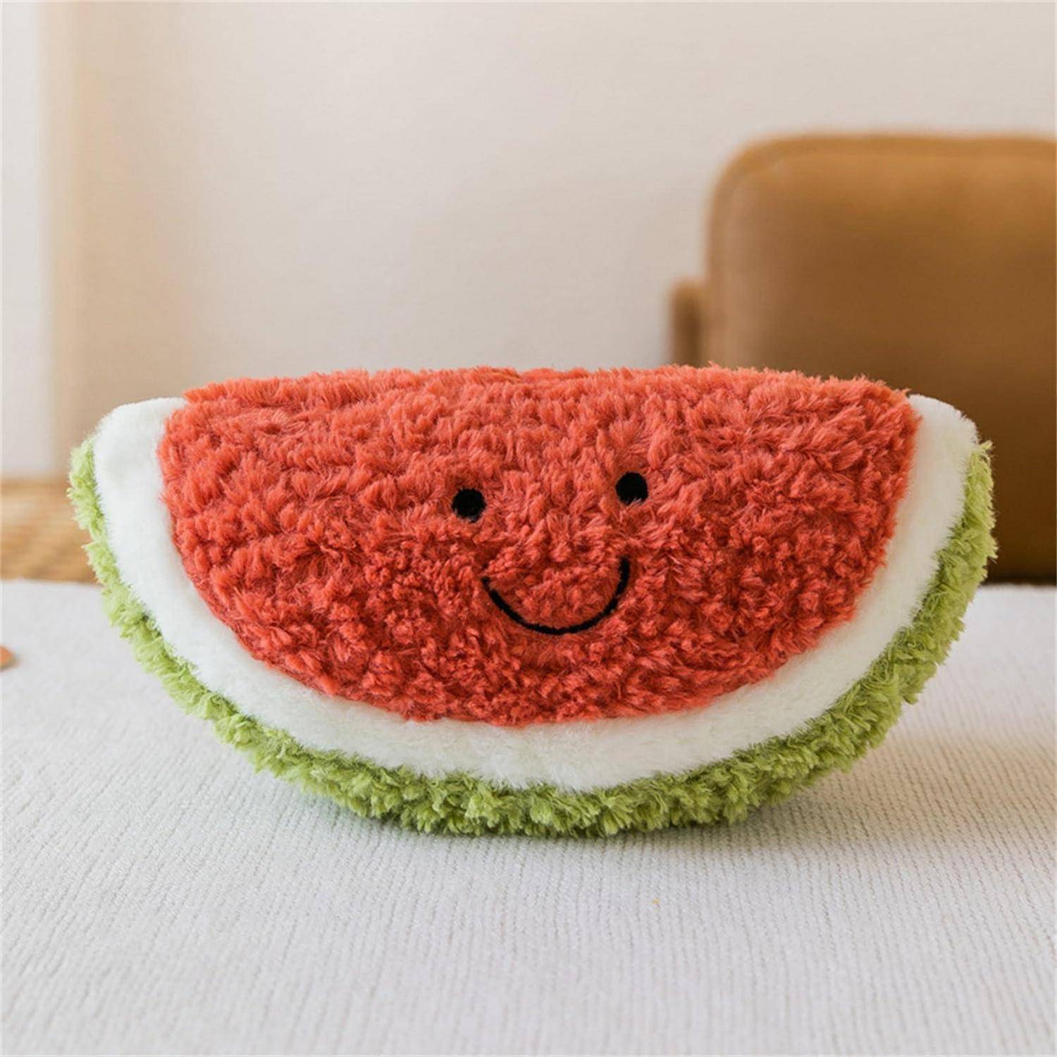 Ein kuscheliges Wassermelonen-Scheiben-Kissen mit einem lachenden Gesicht sitzt auf einer weißen Oberfläche im Innenbereich.