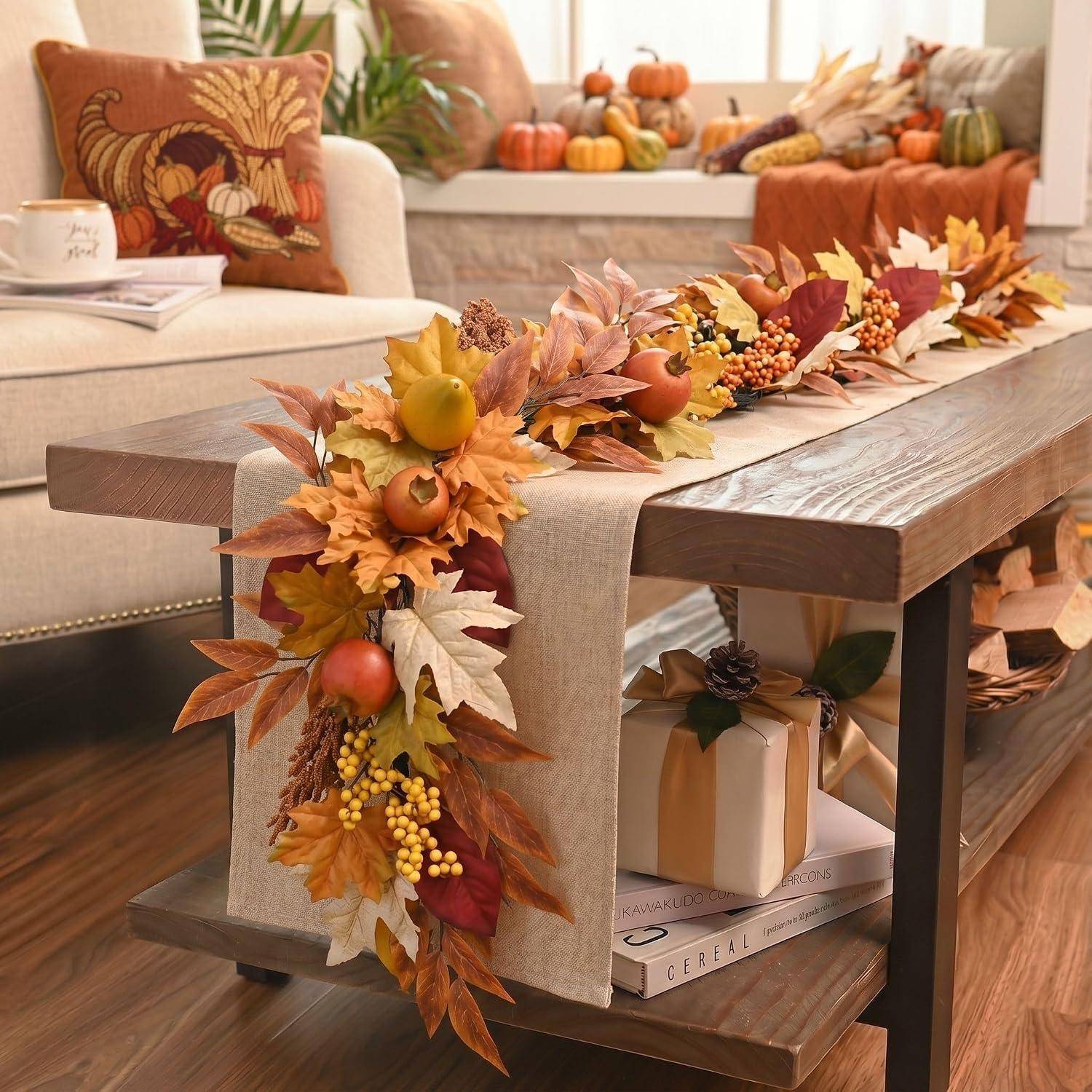 Herbstlich dekorierter Wohnzimmertisch mit einer Blattgirlande, Kürbissen, Fruchtakzenten und verpackten Geschenkboxen darunter.
