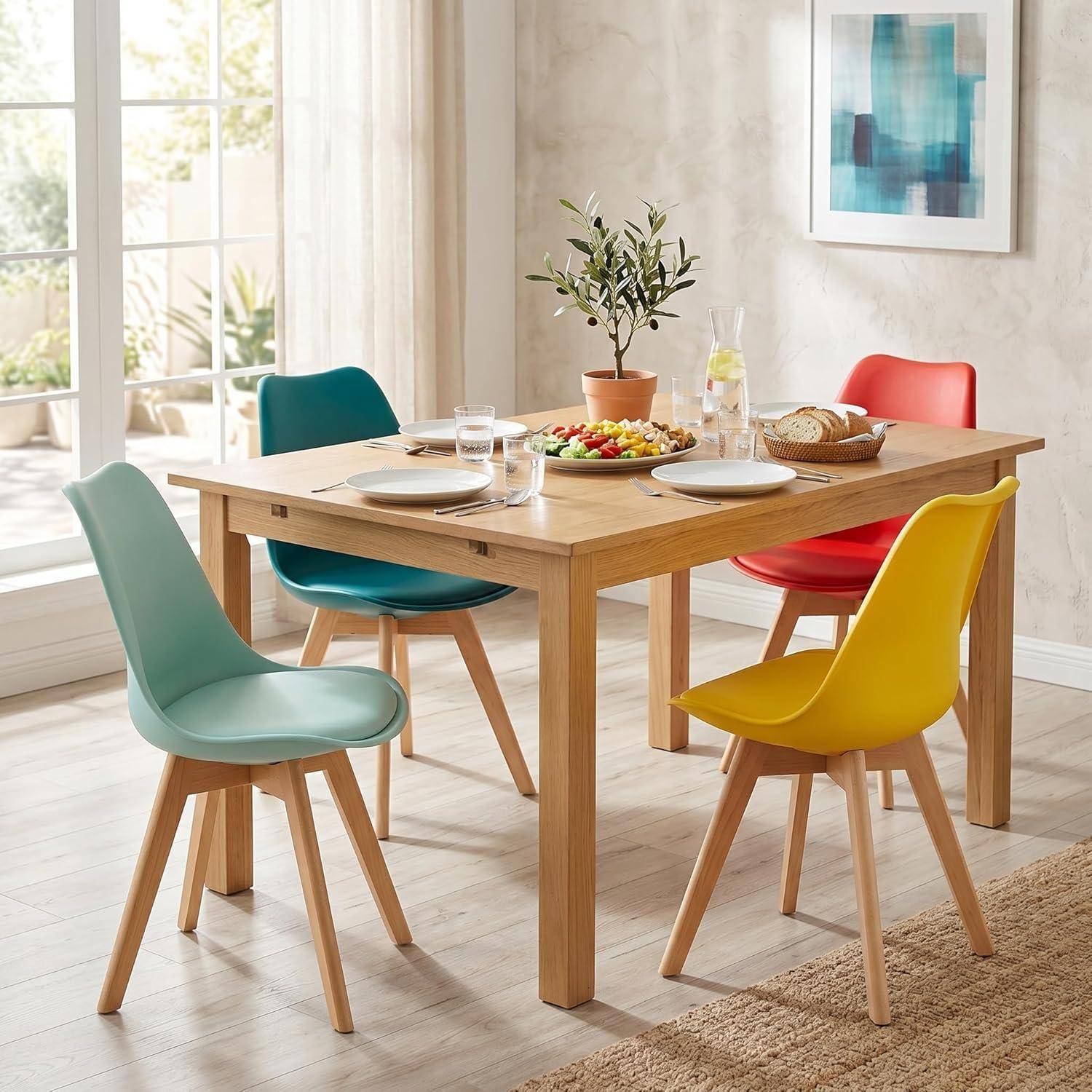 Modernes Esszimmer mit einem Tisch aus hellem Holz, gedeckt für vier Personen, umgeben von farbenfrohen Stühlen in Teal, Rot, Gelb und Mintgrün.