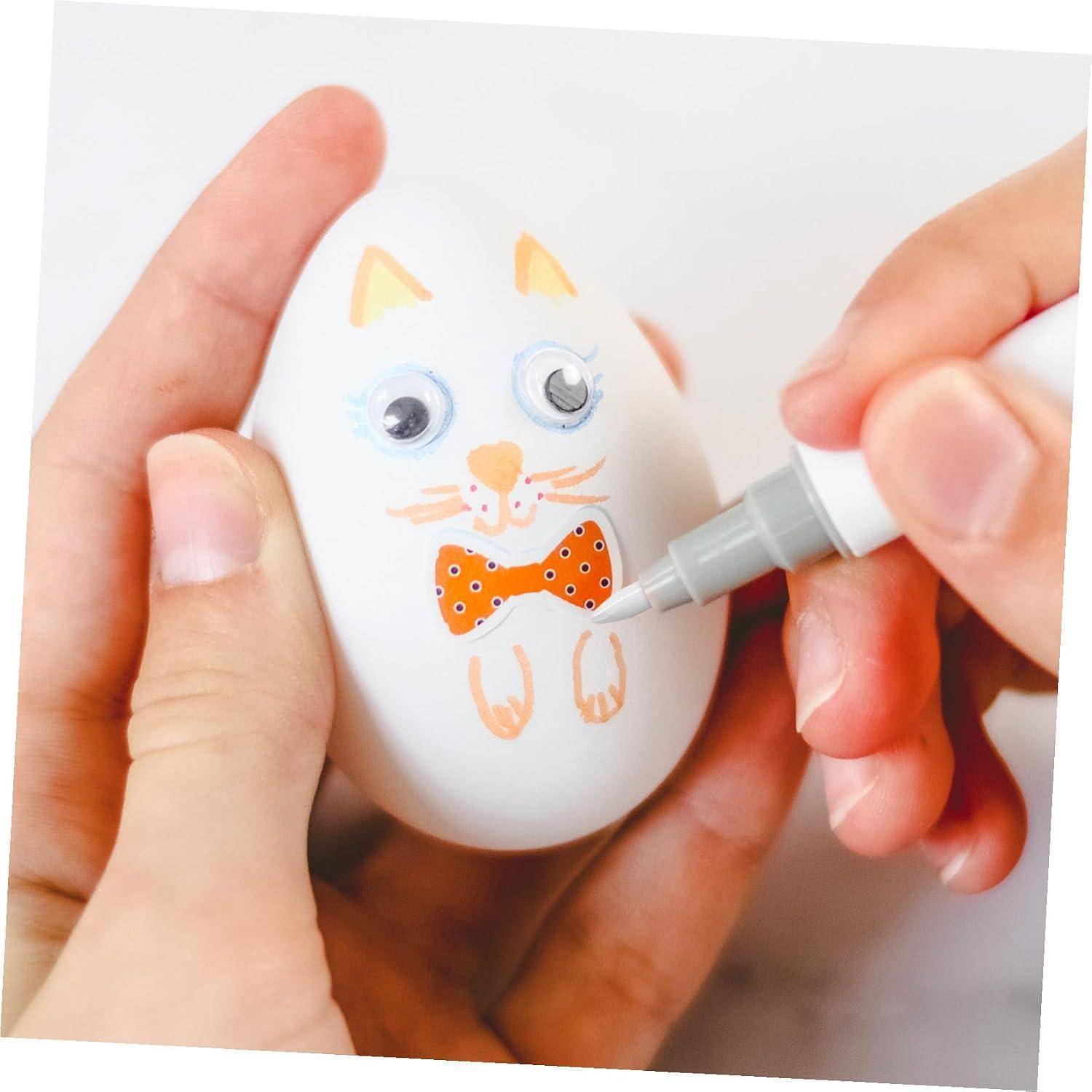 Hände dekorieren ein weißes Ei mit einem Katzengesicht mit einem Marker und fügen Details zu einem kleinen Bastelprojekt hinzu.