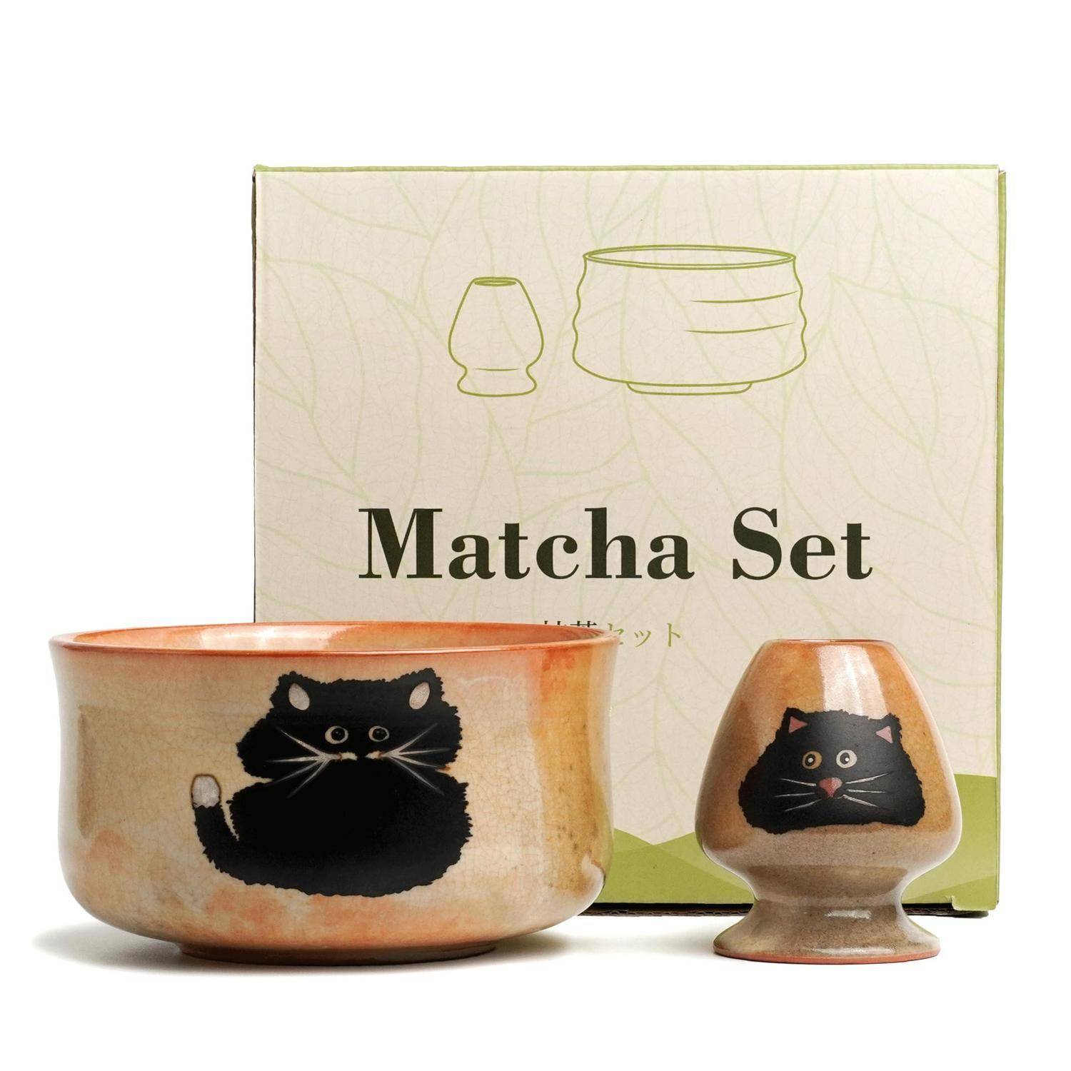 Matcha-Set mit einer Schale und einem kleinen Whisk-Ständer, beide mit schwarzen Katzengesichtern verziert, gezeigt vor der Produktbox.