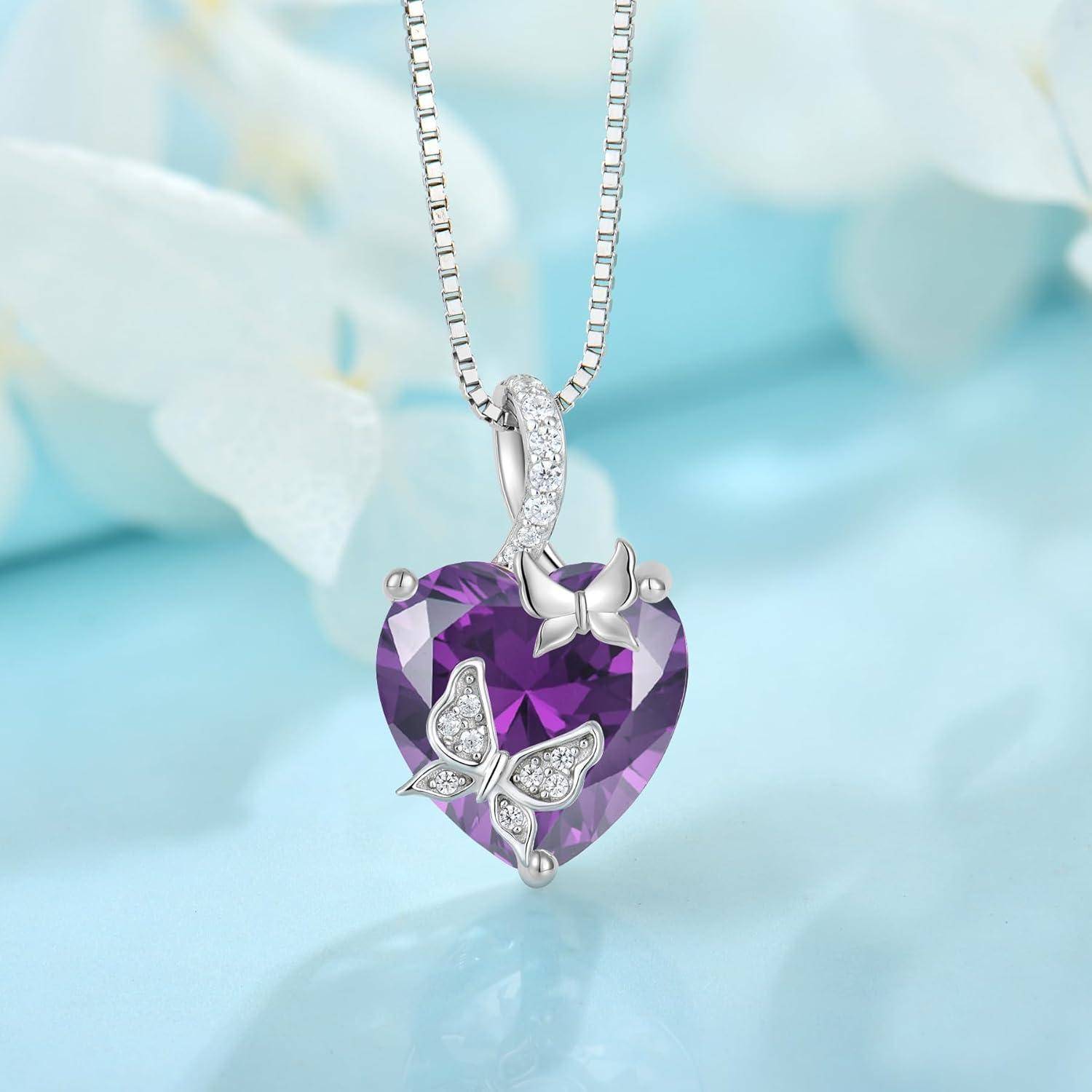 Silberkette mit einem violetten facettierten Herzanhänger, verziert mit zwei Schmetterlingsaksenten, auf weichem blauem Hintergrund gezeigt.