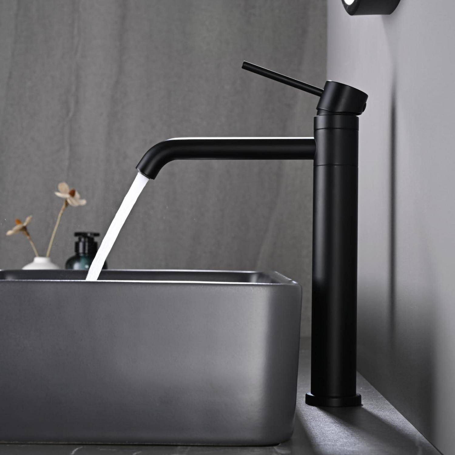 Schwarzer moderner Wasserhahn im Badezimmer, der Wasser in ein rechteckiges graues Waschbecken gegen eine graue Wand gießt.