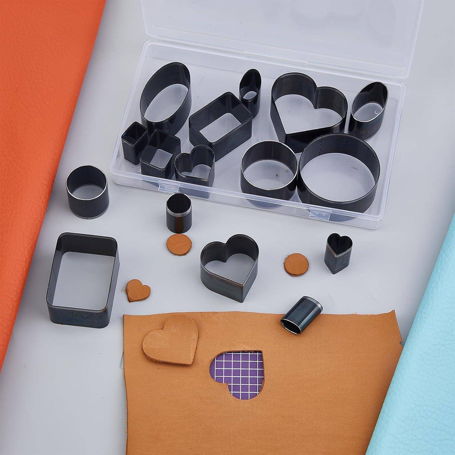 Sortierte schwarze Metallplätzchenformen in einer Kunststoff-Aufbewahrungsbox, mit mehreren Formen und gestempelten Herzformen auf Papier und Stoff darunter.
