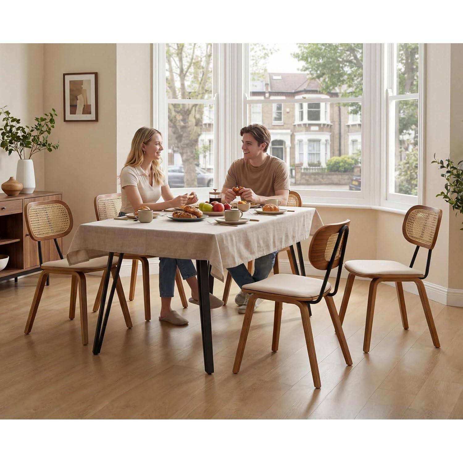 Ein Mann und eine Frau sitzen an einem Esstisch in einem hellen Raum und essen Frühstück oder Brunch vor großen Fenstern.