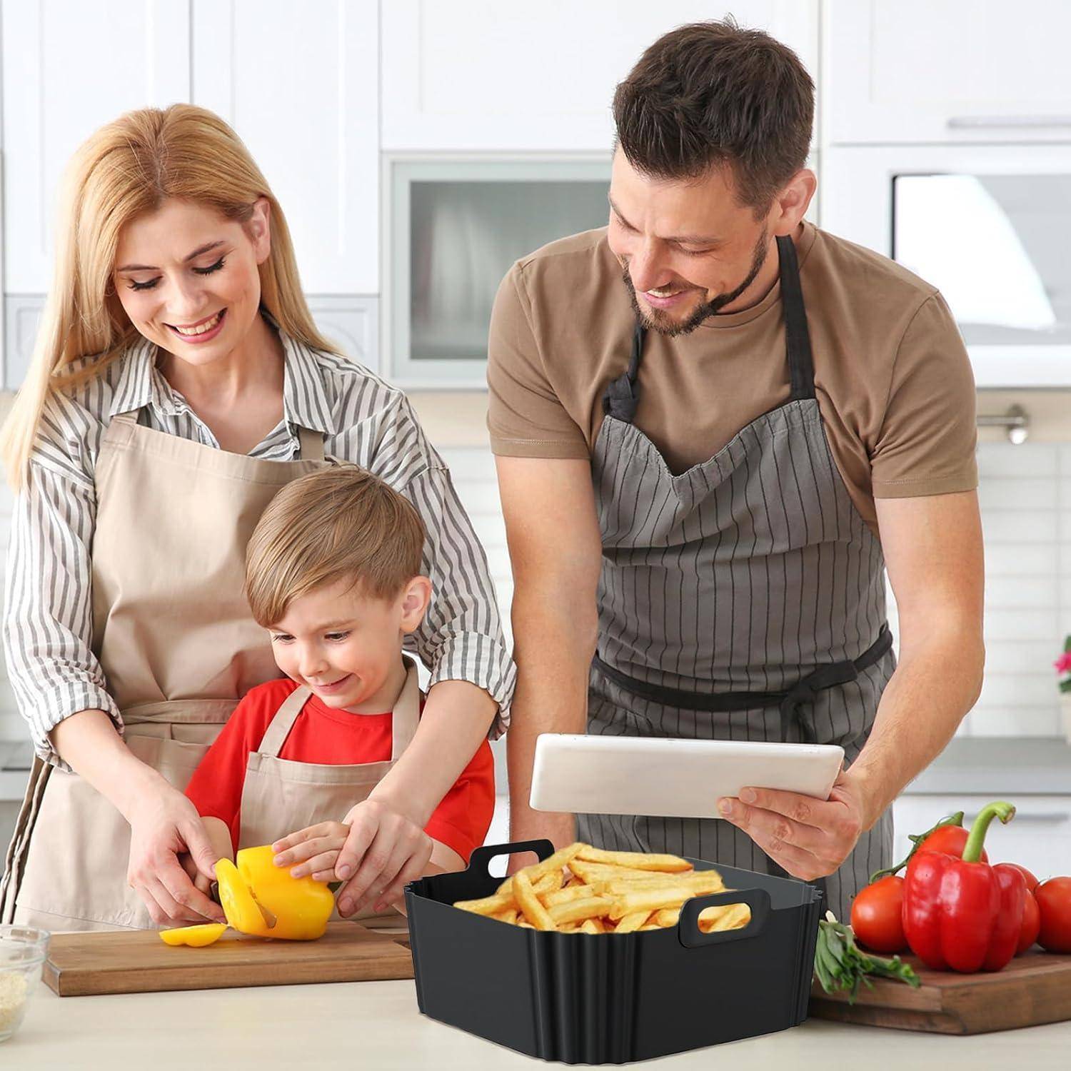 Familie kocht zusammen in einer Küche: Eltern und Kind schneiden eine gelbe Paprika, während ein Mann ein Tablet neben einem Korb mit Pommes und frischem Gemüse hält.