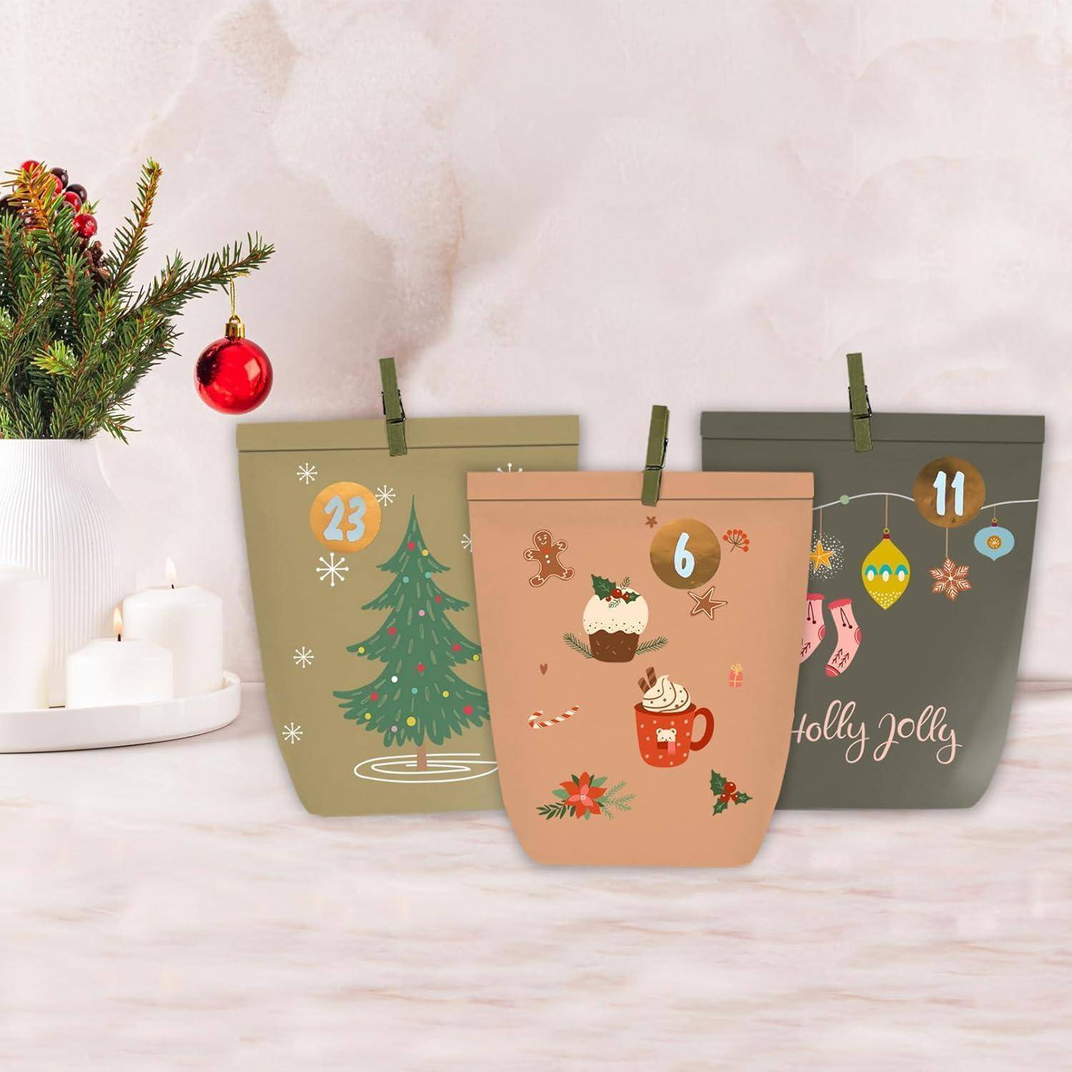 Drei festliche Weihnachts-Papiergiftbags in Grün, Pfirsich und Grau mit Wäscheklammern, verziert mit Weihnachtssymbolen und den Zahlen 23, 6 und 11.