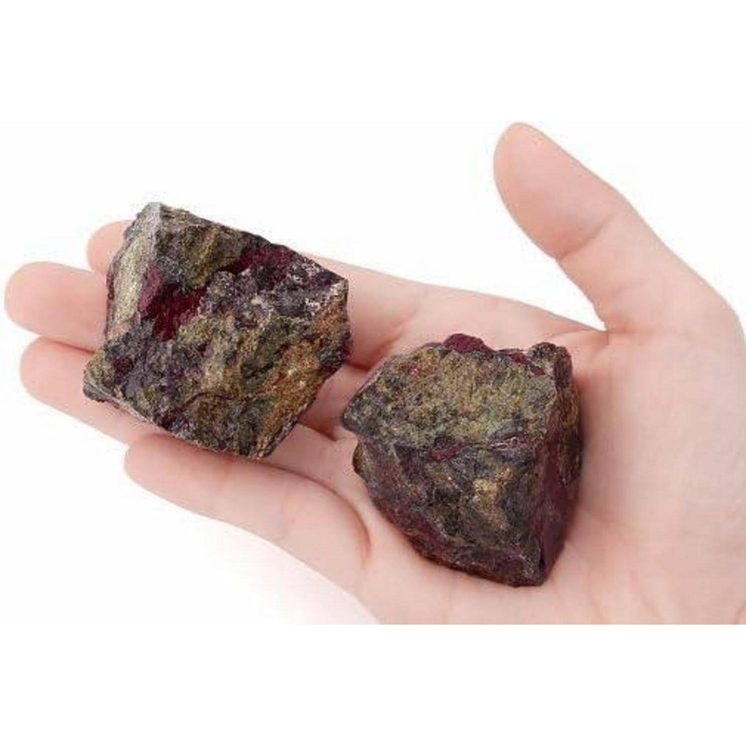 Eine Hand hält zwei raue, dunkle Mineralsteine gegen einen einfachen weißen Hintergrund.