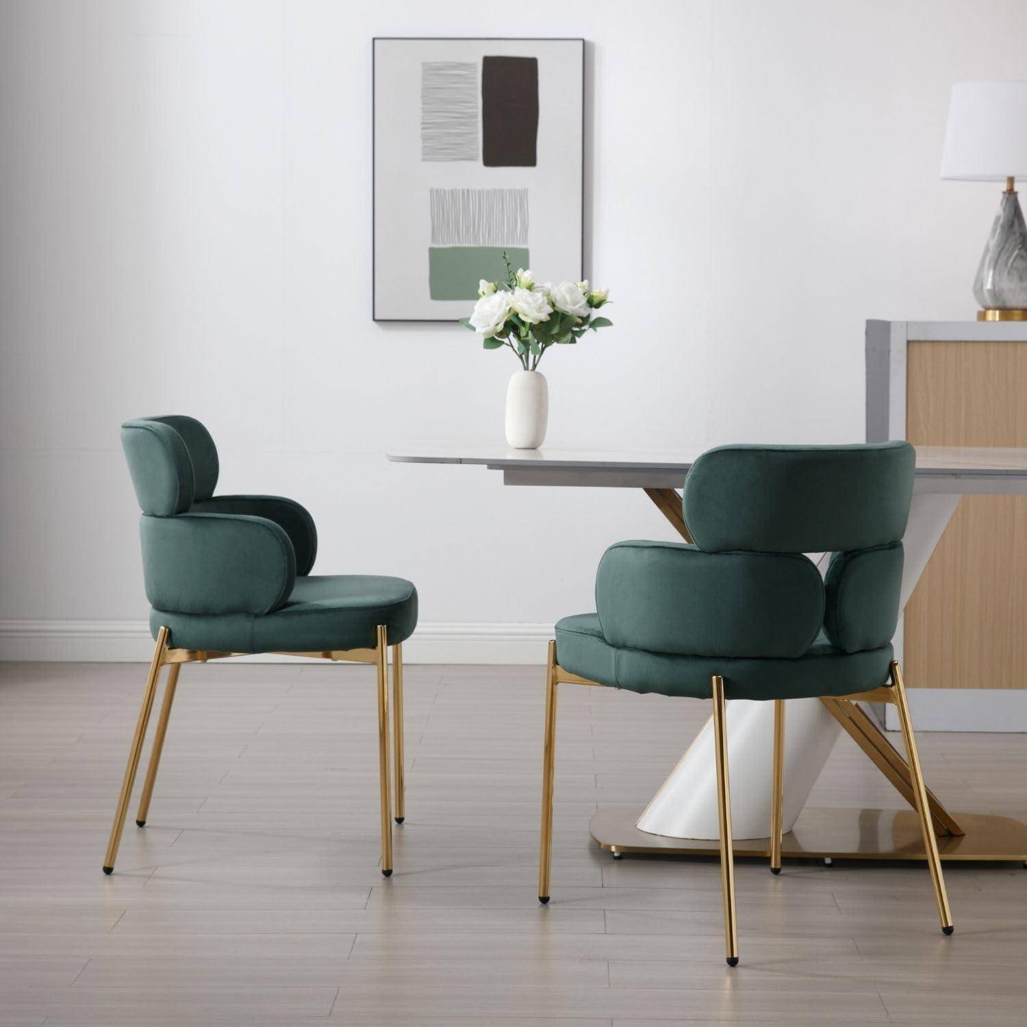Moderner Essbereich mit zwei grün gepolsterten Stühlen, einem Tisch mit weißen Blumen, Wandkunst und einem Sideboard in einem minimalistischen Raum.