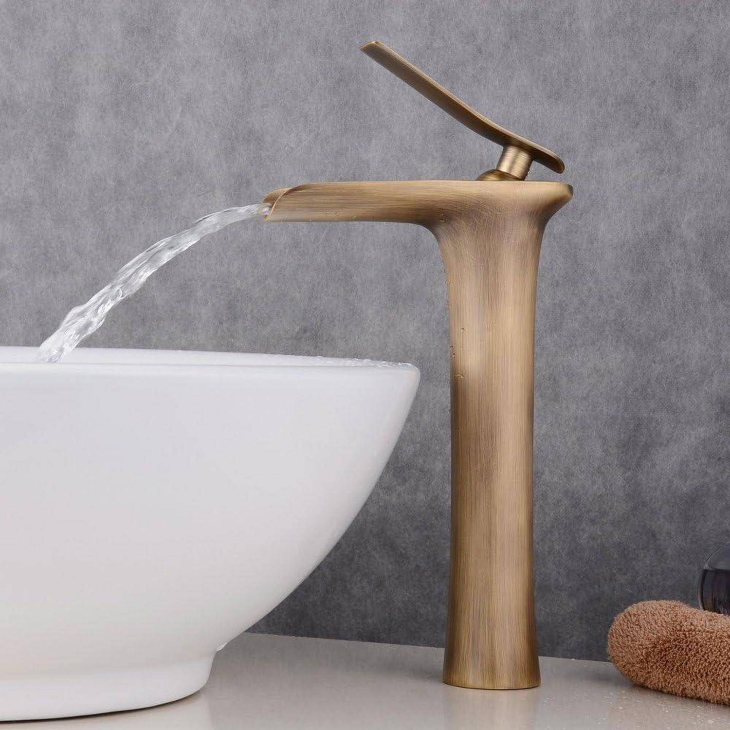 Moderner Bronzehahn mit fließendem Wasser in ein weißes Waschbecken vor einer grauen Wand.