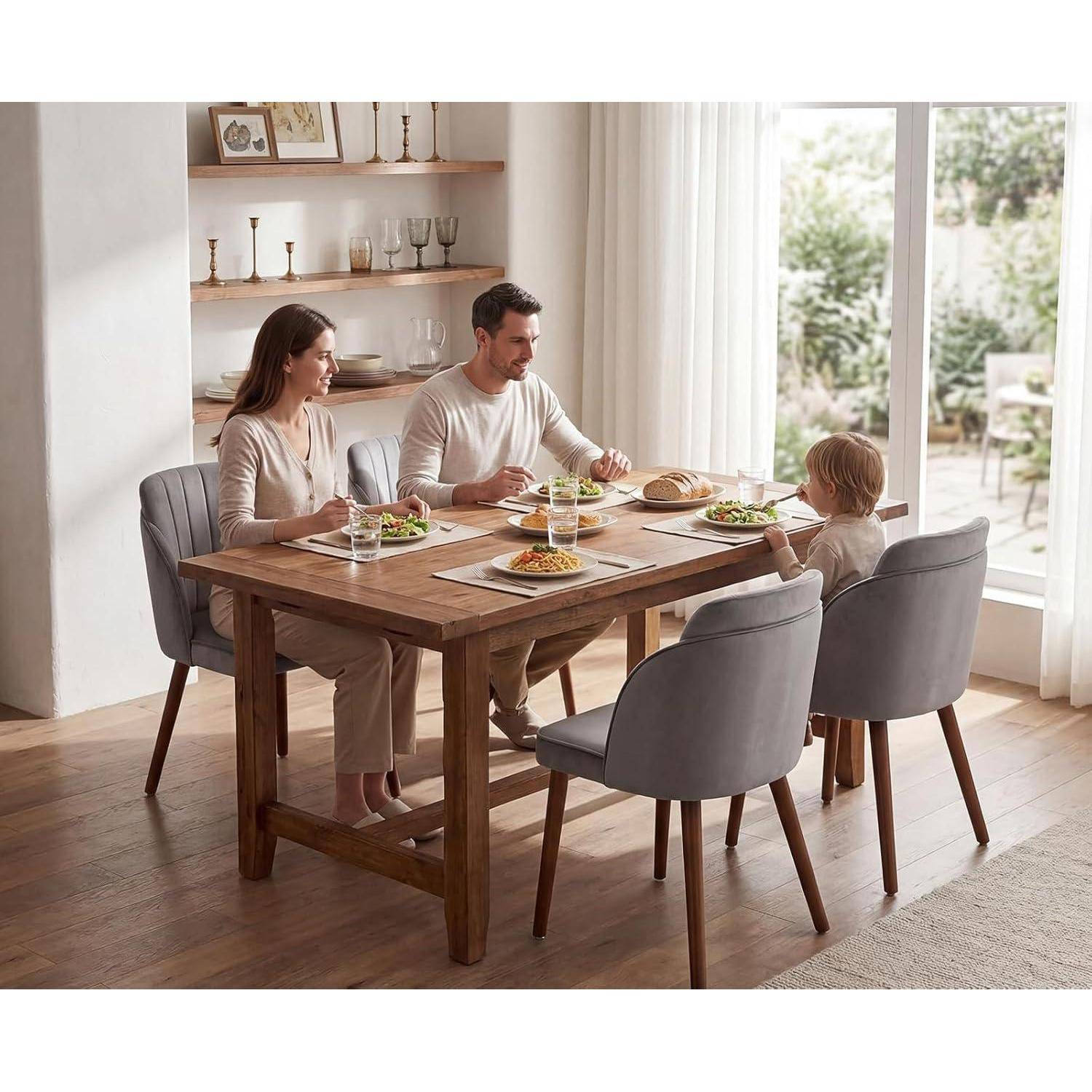 Familie aus drei Personen, die mittags an einem Holzesstisch in einem hellen Zuhause essen, mit Tellern voller Essen und Licht von einem großen Fenster.
