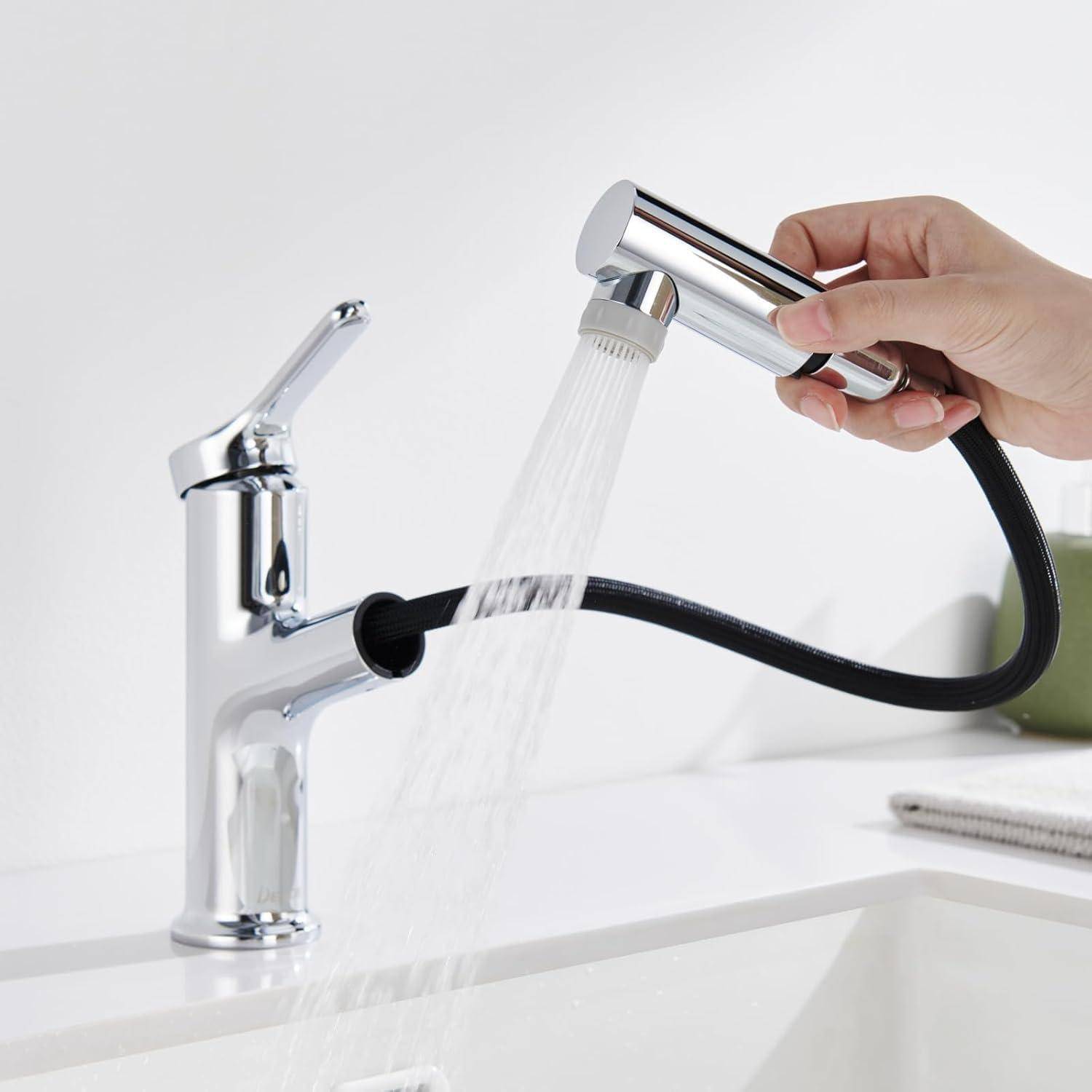 Hand, die einen verchromten Ausziehsprüher hält und Wasser in einen modernen Badezimmer-Spülhahn spült.