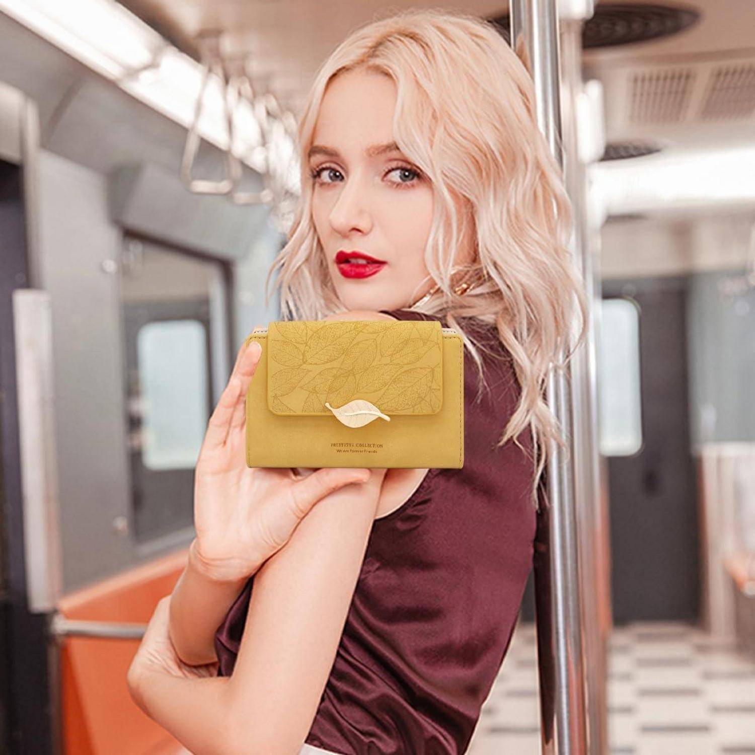 Blonde Frau in einem Bordeauxkleid hält eine kleine gelbe Geldbörse oder Clutch in einem Zug oder einer U-Bahn-Wagen.