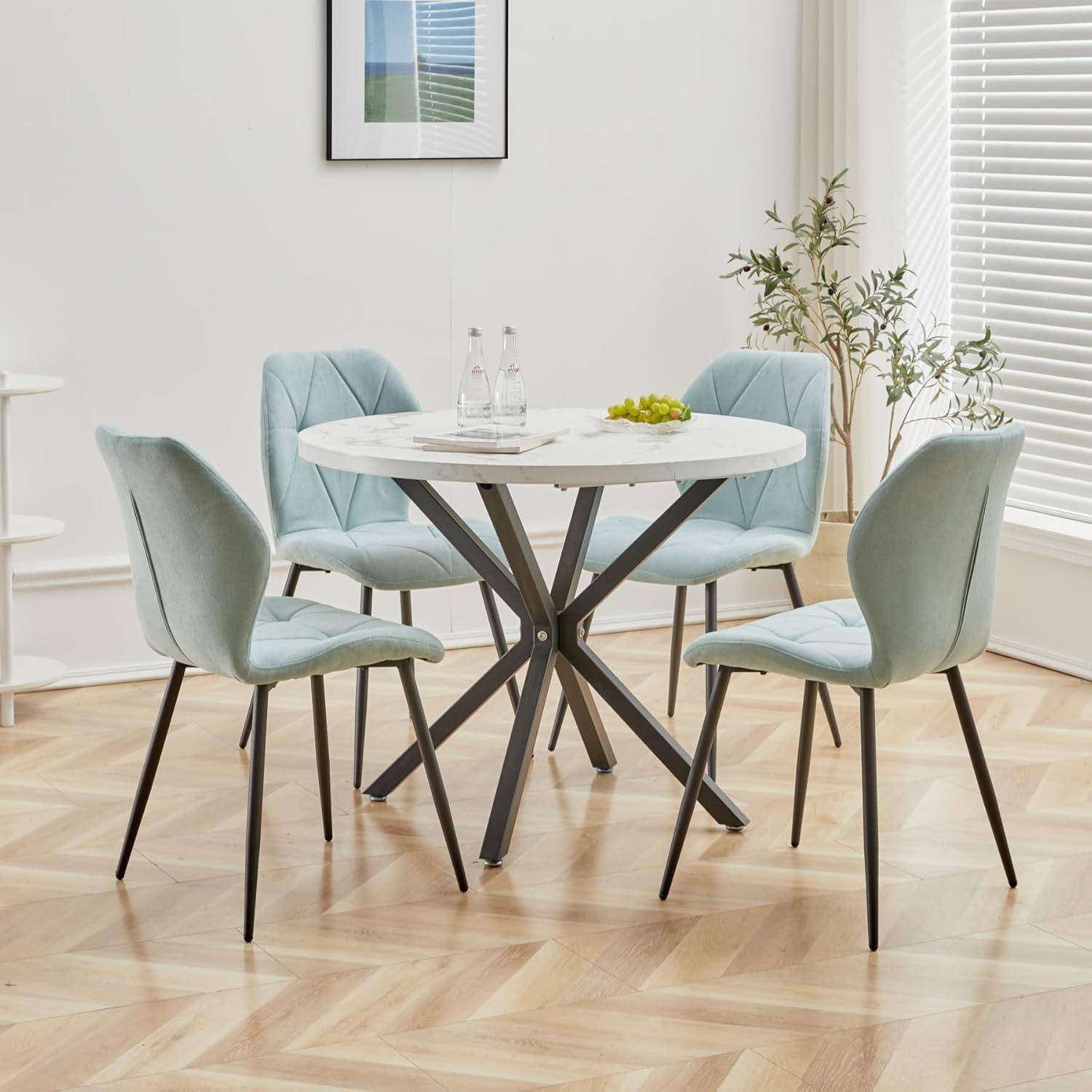 Modernes Esszimmer-Set mit einem runden weißen Tisch und vier hellblauen gepolsterten Stühlen in einem hellen Raum.