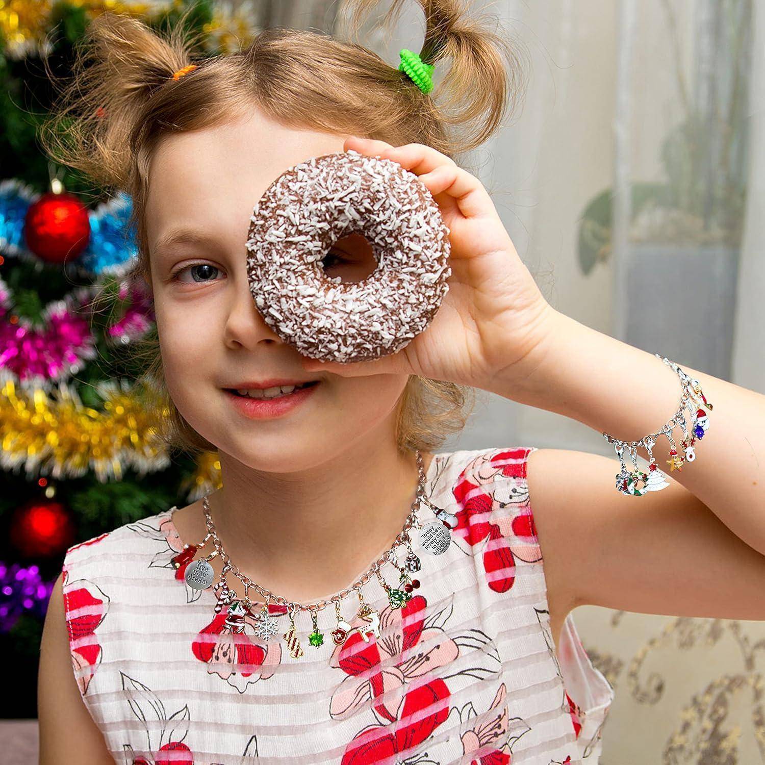 Ein junges Mädchen hält einen mit Schokoladenstreuseln bestäubten Donut über ein Auge wie ein Monokel und lächelt neben einem geschmückten Weihnachtsbaum im Innenraum.