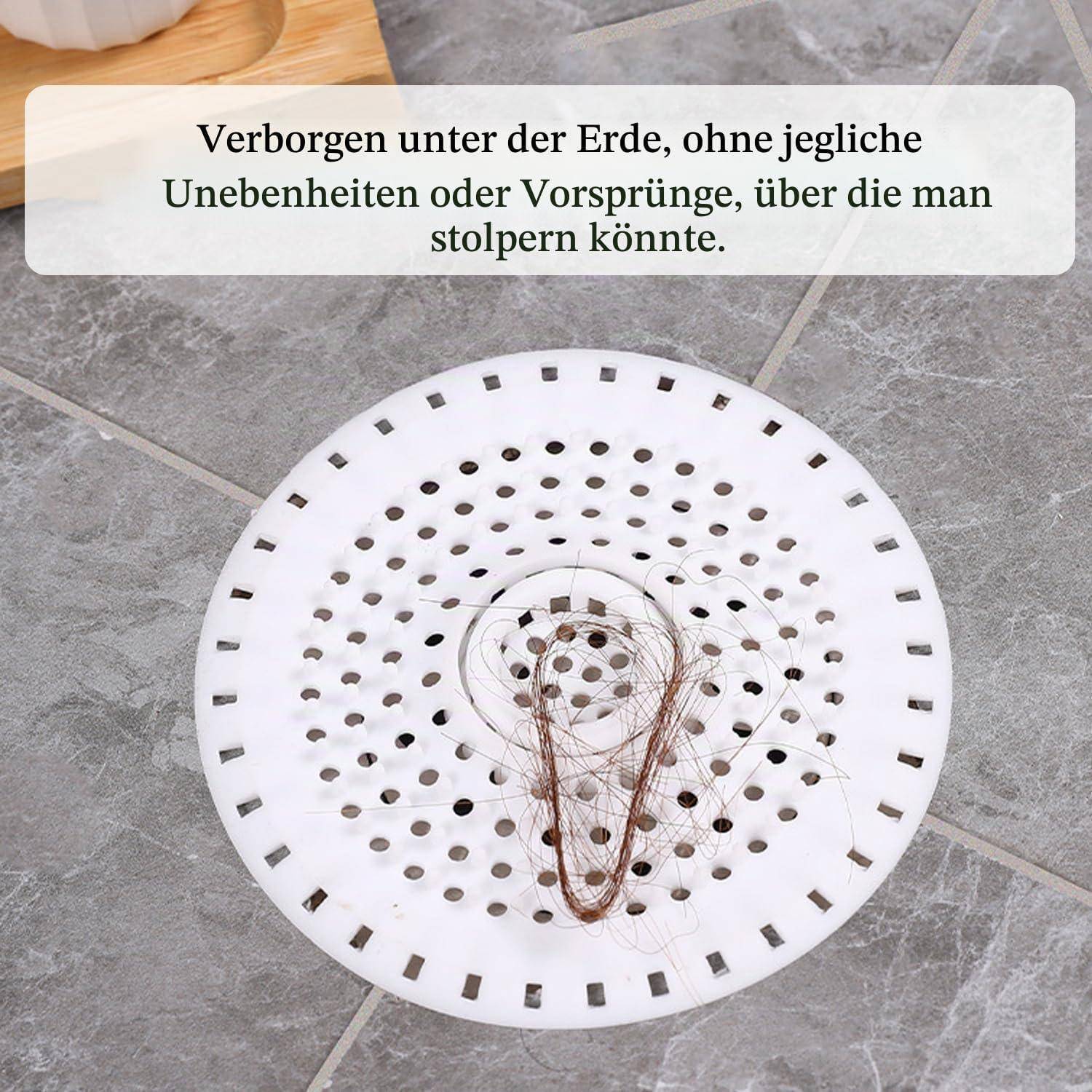 Runde weiße Bodenablaufabdeckung bündig in grauem Fliesenbelag eingelassen; überlagerte deutsche Textzeile besagt, dass sie unterirdisch verborgen, ebenerdig und trittsicher ist.