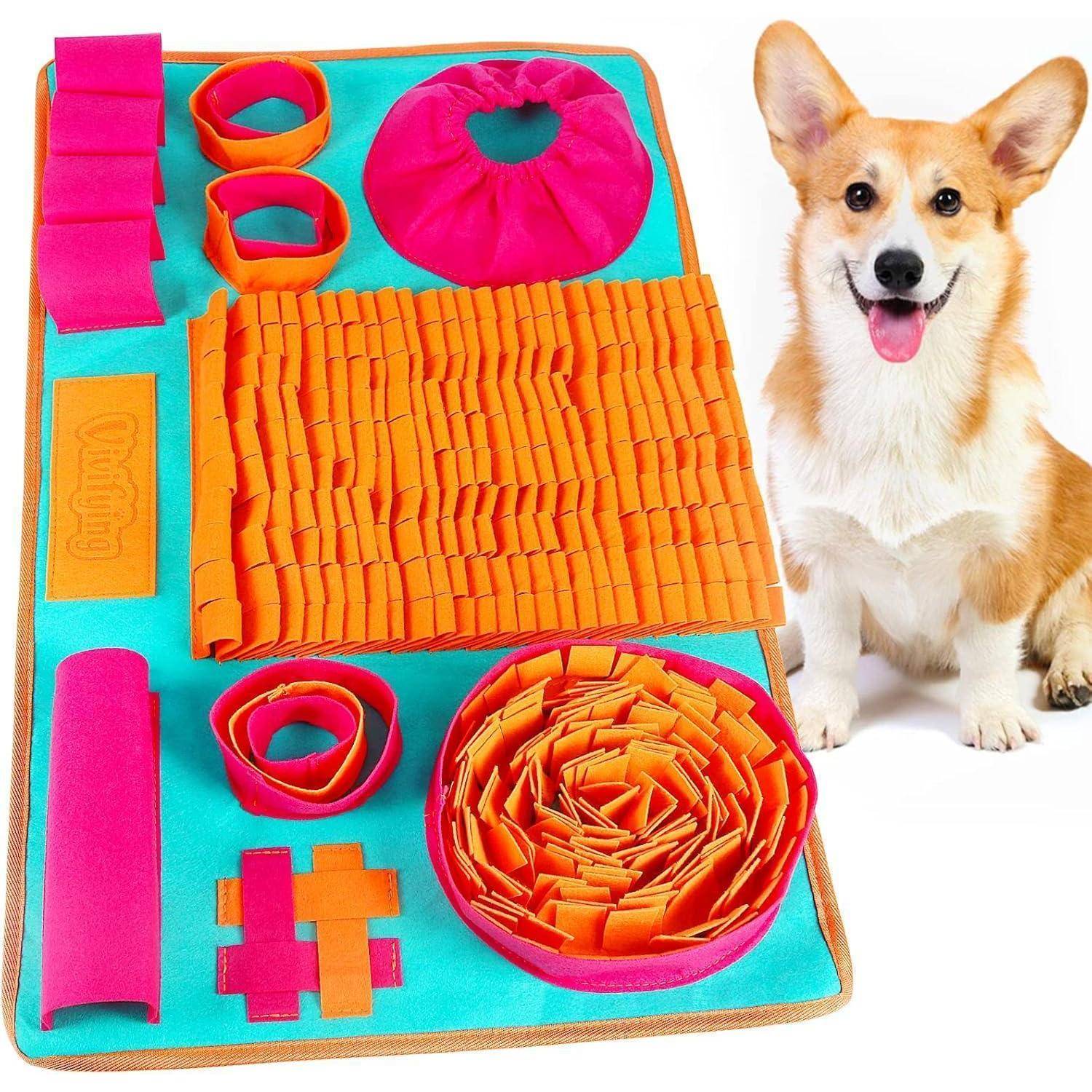 Ein glücklicher Corgi sitzt neben einer bunten Hundepuzzle-Matte mit Stofffalten und Futterversteck-Fächern.