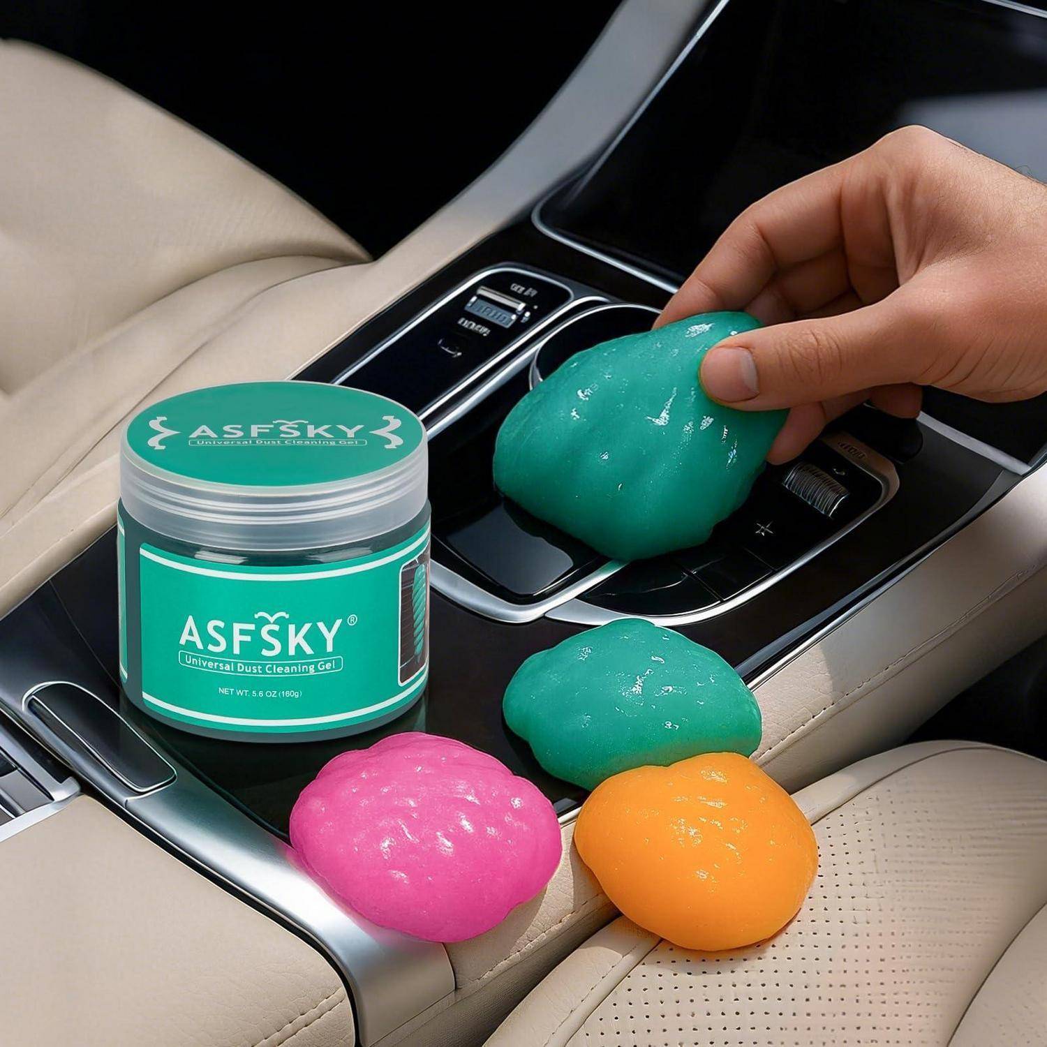 Dose mit ASFSKY-Autoreinigungs-Gel neben farbigen Gel-Klumpen in einer Mittelkonsole eines Autos, mit einer Hand, die das türkisfarbene Gel verwendet, um Staub und Verschmutzung aufzusammeln.