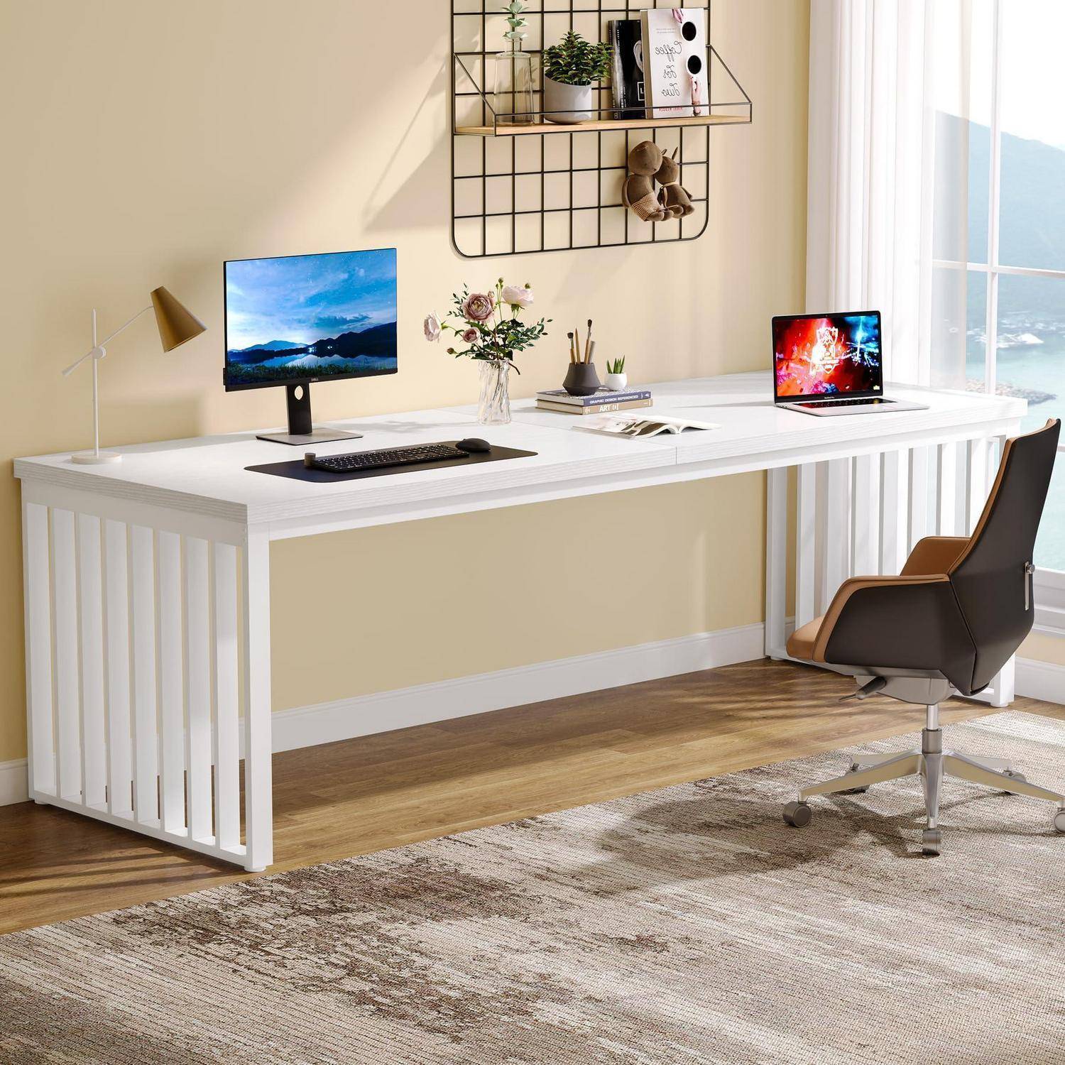 Helles modernes Homeoffice mit einem langen weißen Schreibtisch, Desktop-Monitor, Laptop, schwarzem Stuhl, Wandregal und Dekoration in der Nähe eines Fensters mit Meeresblick.