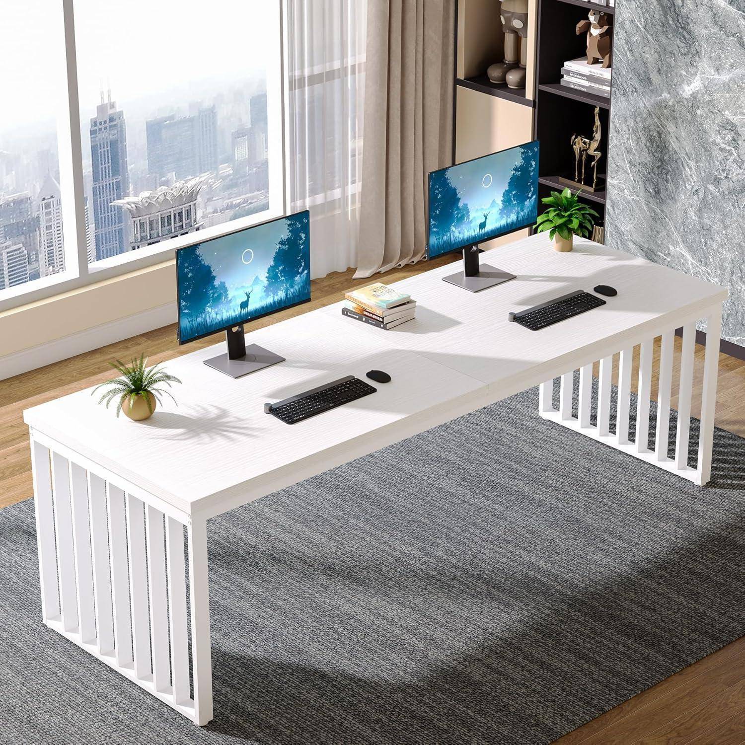 Helle moderne Gemeinschaftsarbeitsstation mit einem langen weißen Schreibtisch, zwei Monitoren, Tastaturen, Mousepads, kleinen Pflanzen, Büchern und Stadtaussichtsfenstern dahinter.