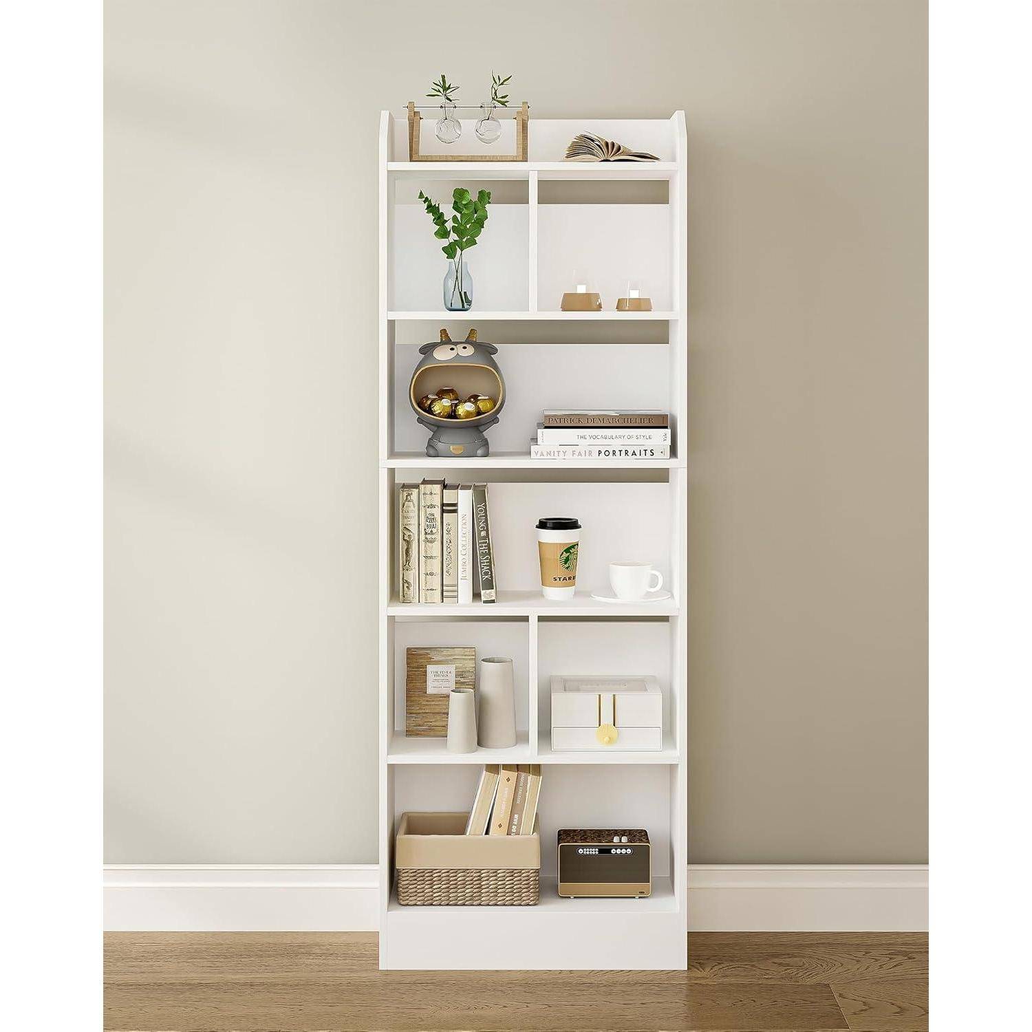 Weißes hohes Bücherregal an einer beigen Wand, stilisiert mit Büchern, einer Vase mit Grünpflanzen, Kerzen, einer Kaffeetasse, Aufbewahrungskörben und dekorativen Objekten.