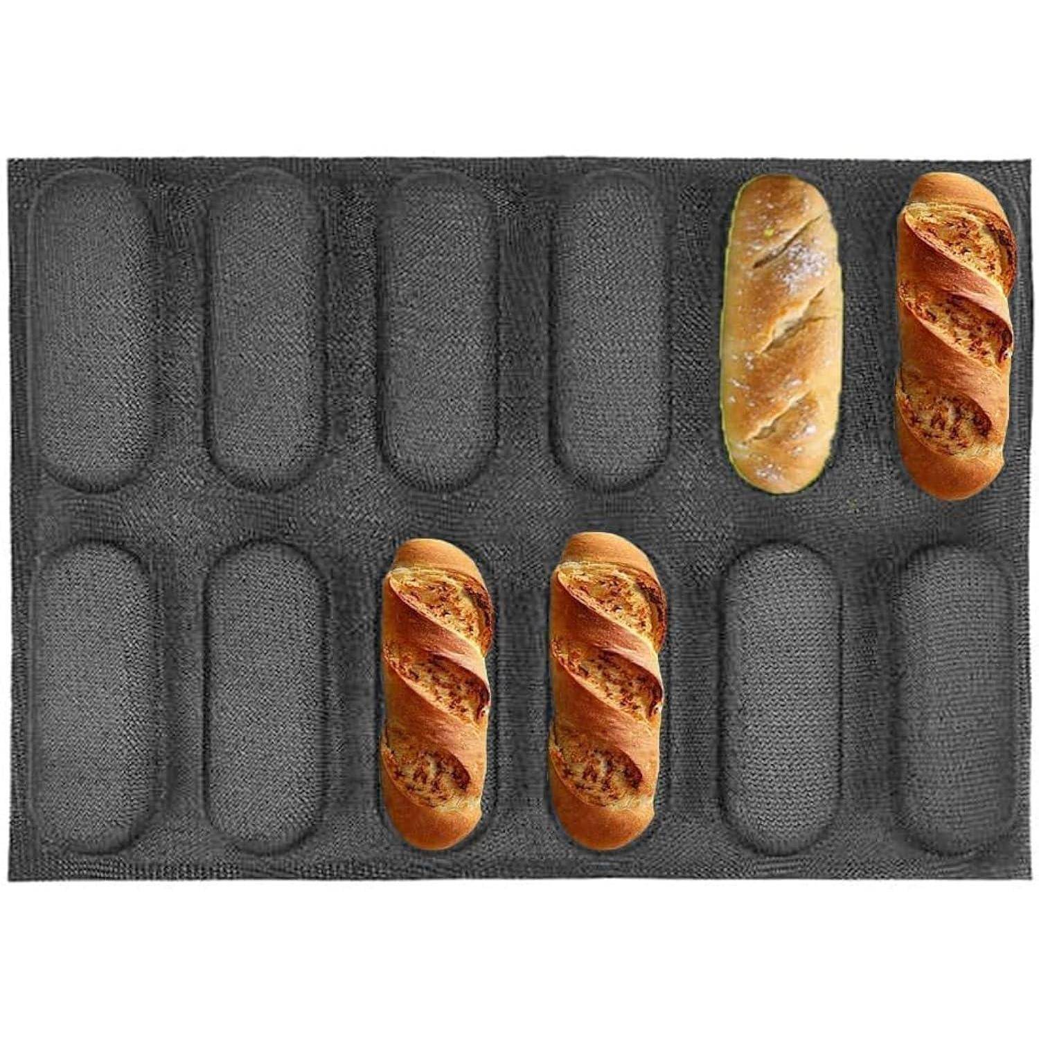 Ein schwarzes Backblech mit acht laibförmigen Vertiefungen, das vier kleine Baguettes hält: zwei oben rechts und zwei in der Nähe der unteren Mittellage.