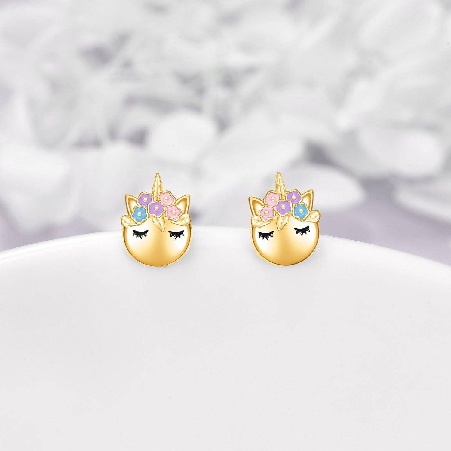 Paar goldener Einhorn-Ohrstecker mit pastellfarbenen Blumenkronen und geschlossenen Augen auf einer weißen Oberfläche.