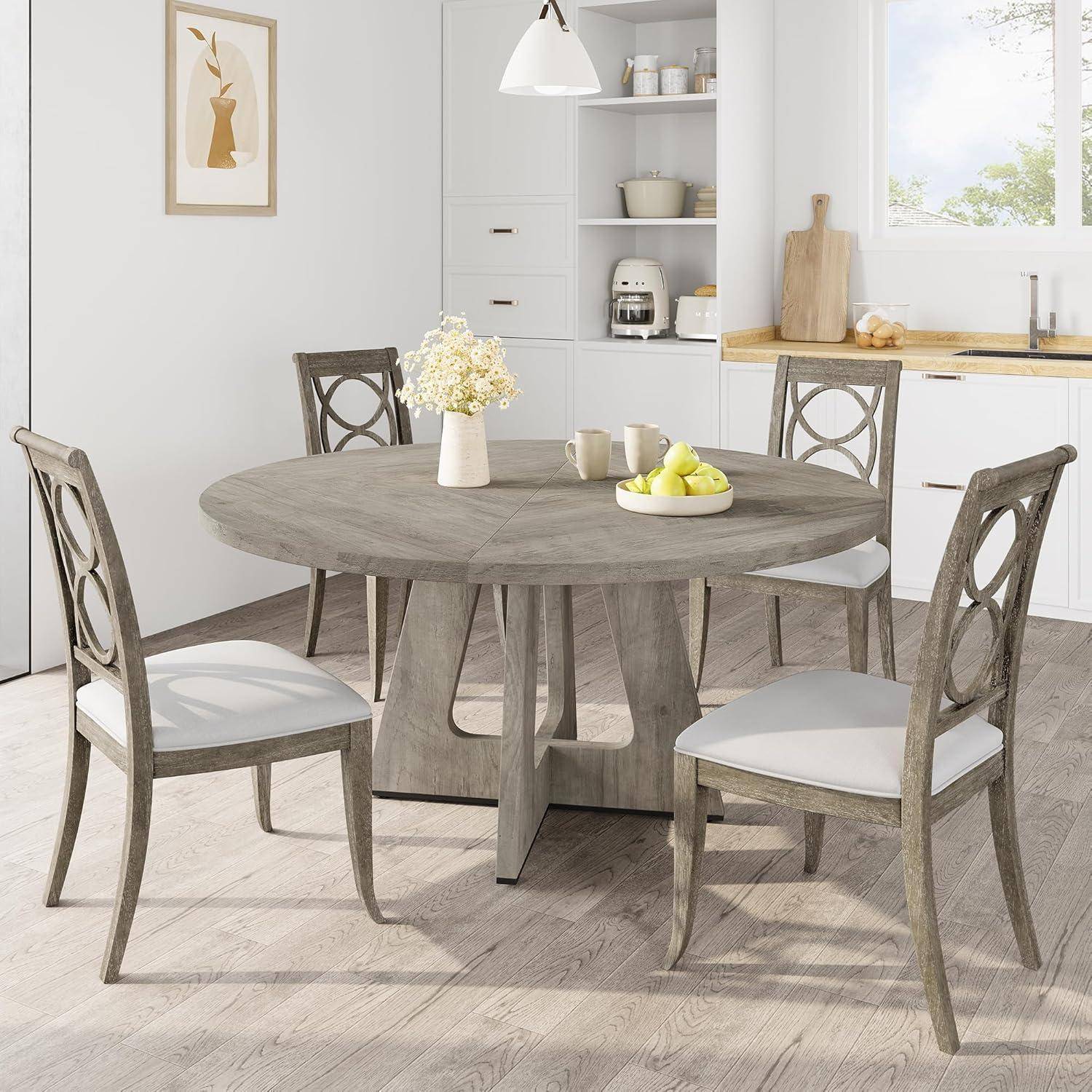 Modernes Esszimmer mit einem runden Holztisch, vier gepolsterten Stühlen und einer Vase und Schüssel als Tischdeko in einem hellen, neutralen Küchenbereich.